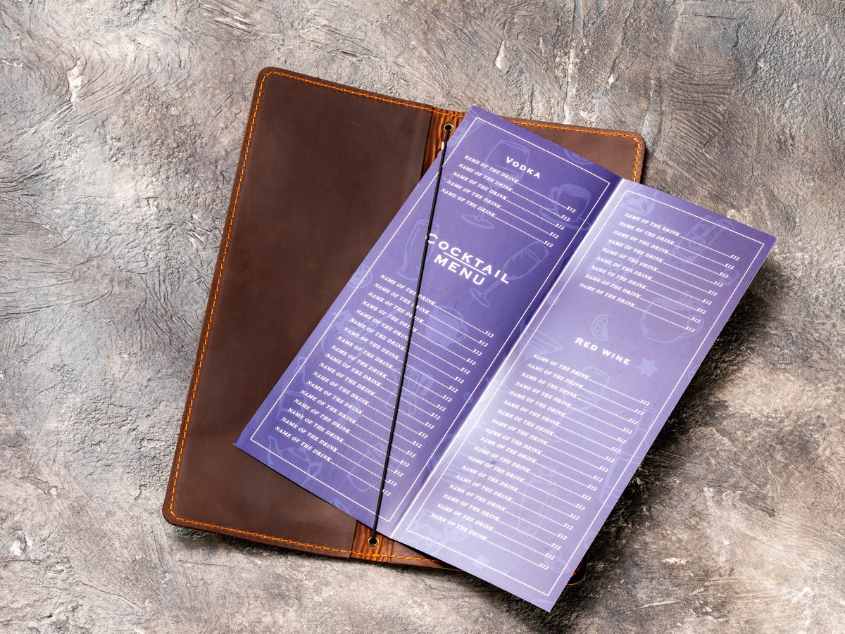 Open brown leather cocktail menu cover with elastic cord holding folded drink and wine menu pages