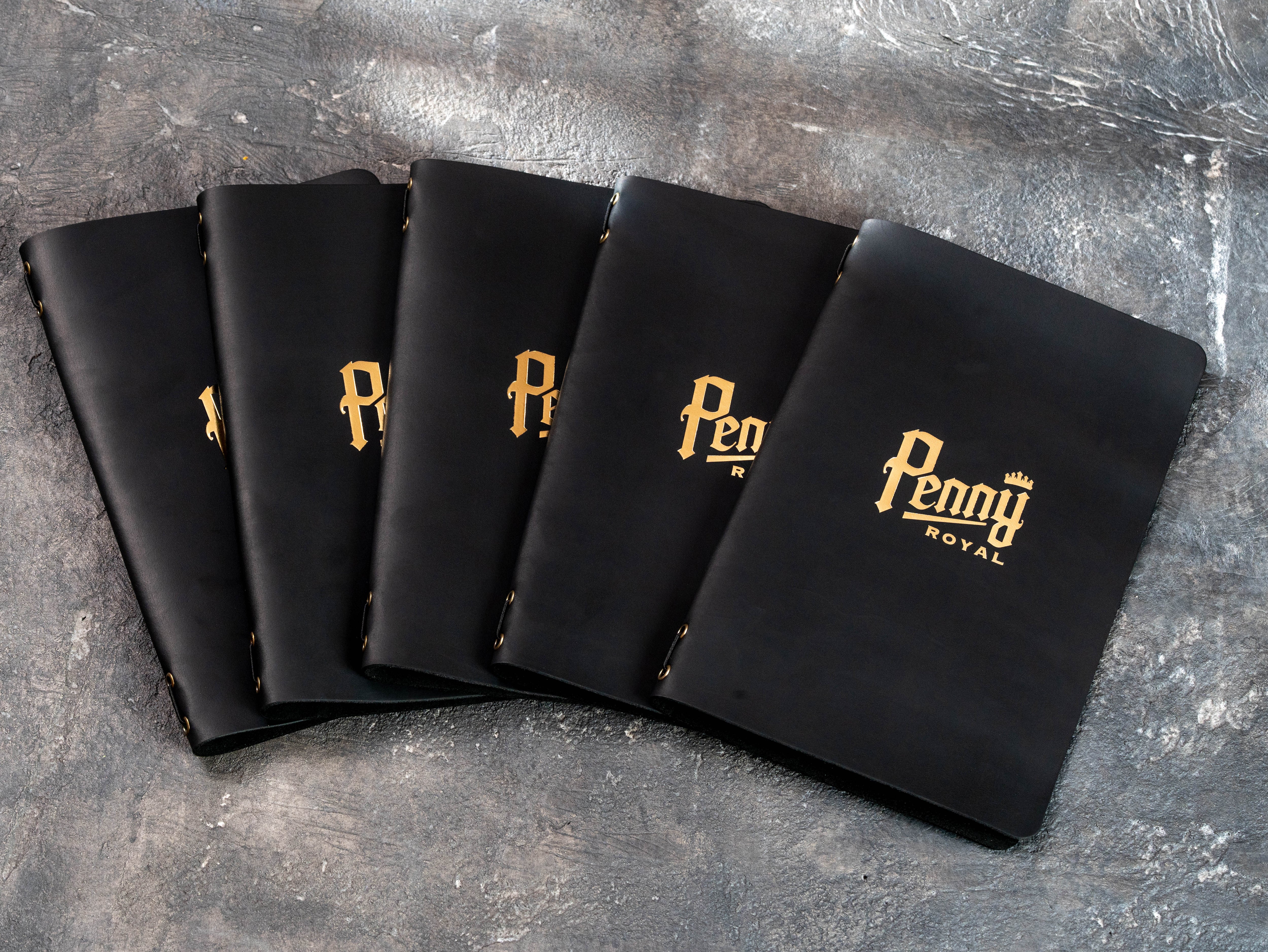 Stack of custom black leather restaurant menu covers made by Mureli Workshop for Penny Royal with gold foil logos