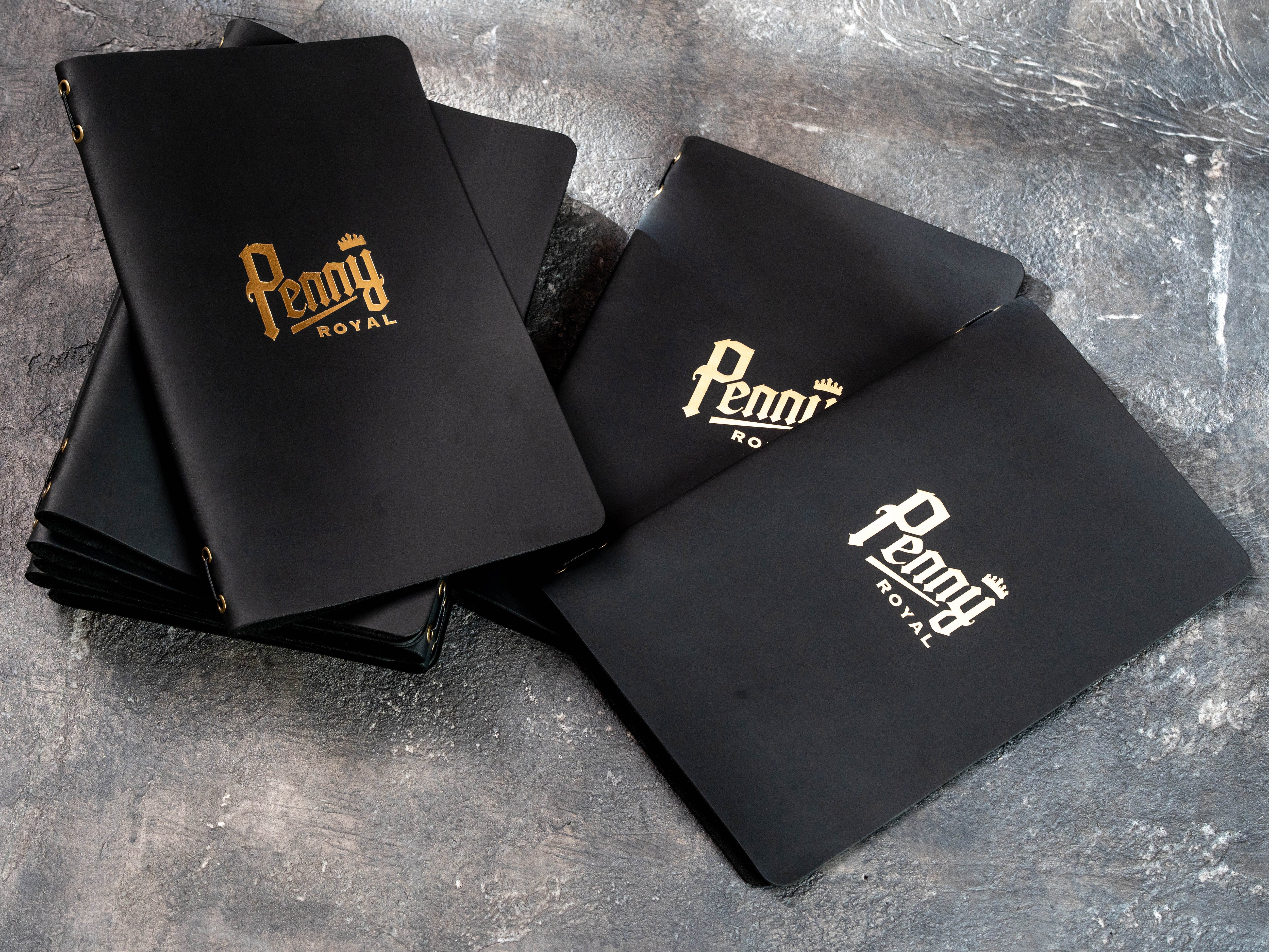 Close-up of black leather restaurant menu cover with Penny Royal logo stamped in gold foil