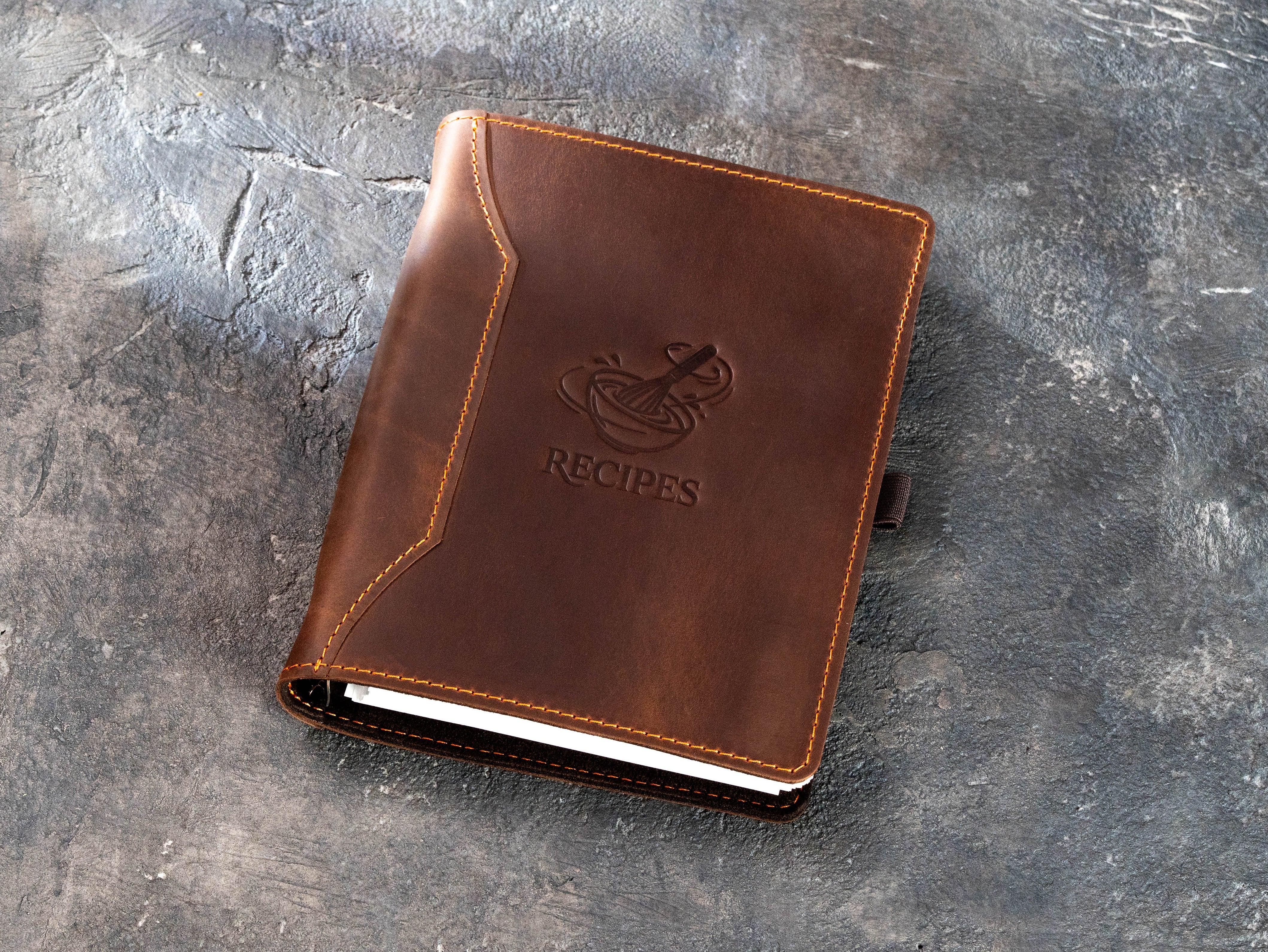 Brown leather 6-ring recipe book with fixed whisk and bowl design, shown in the closed position