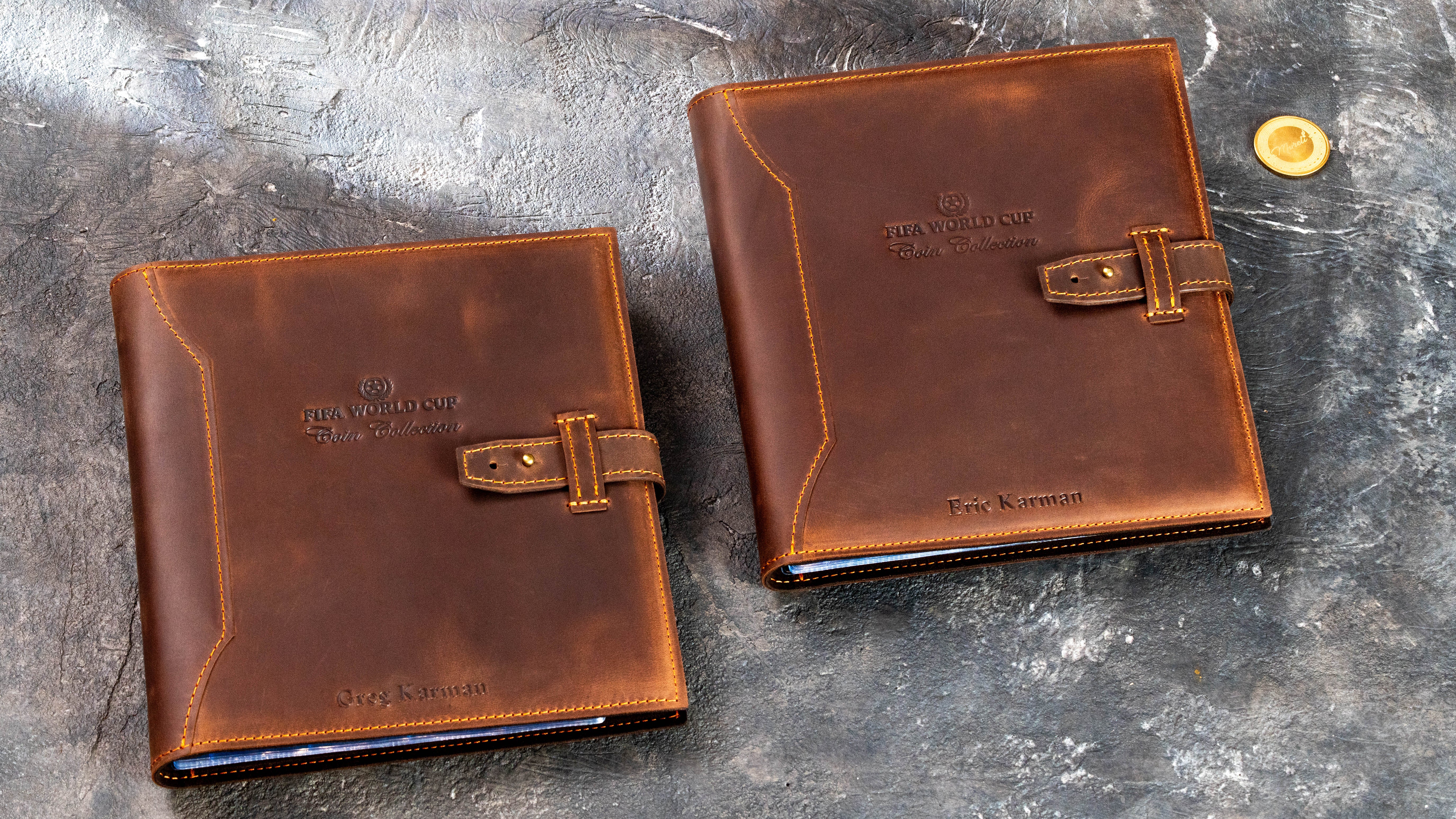 Two personalized brown Crazy Horse leather coin collection albums with strap closures and custom embossed names