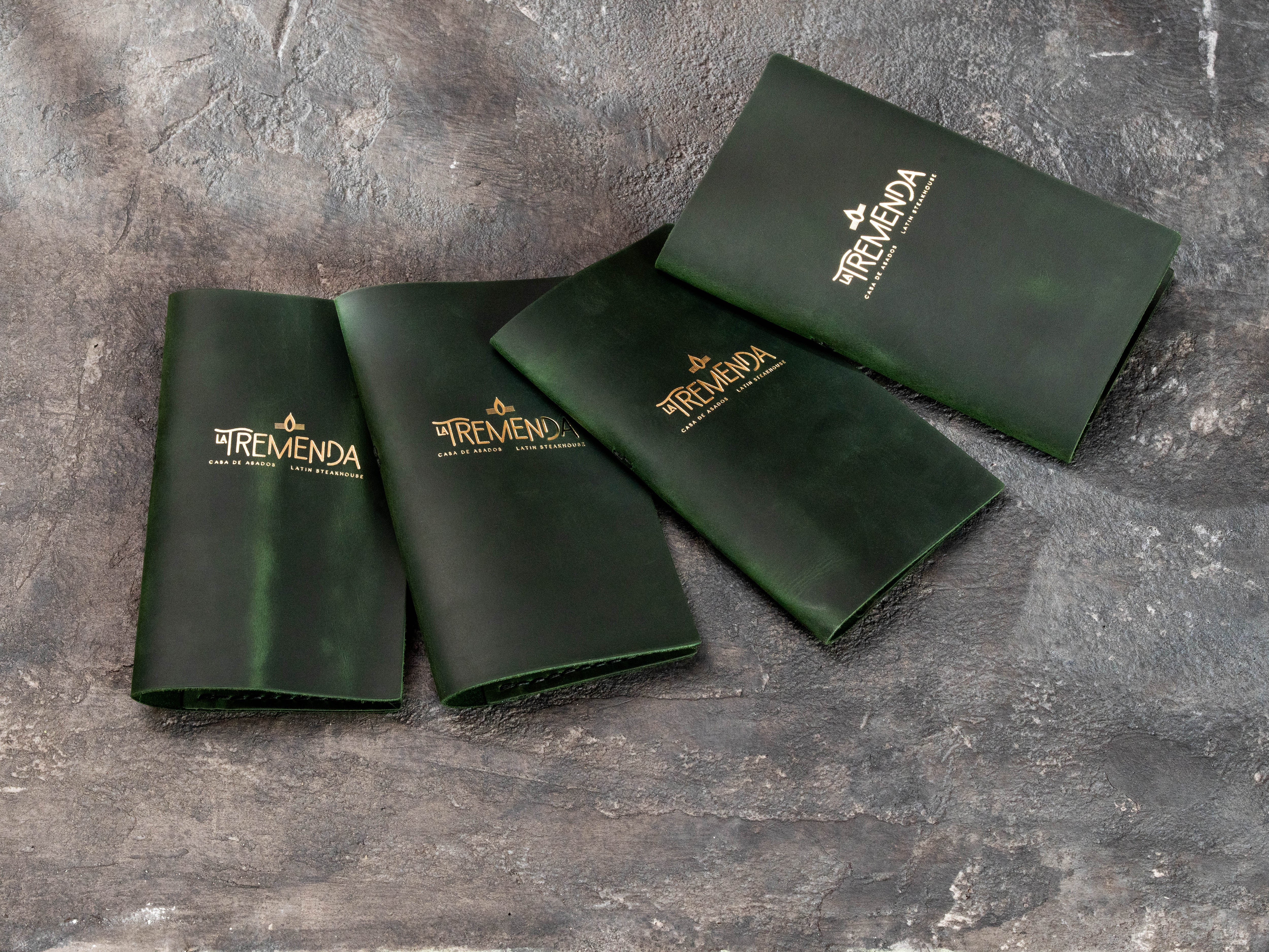 Custom green leather check presenters with gold La Tremenda logo for a Latin steakhouse