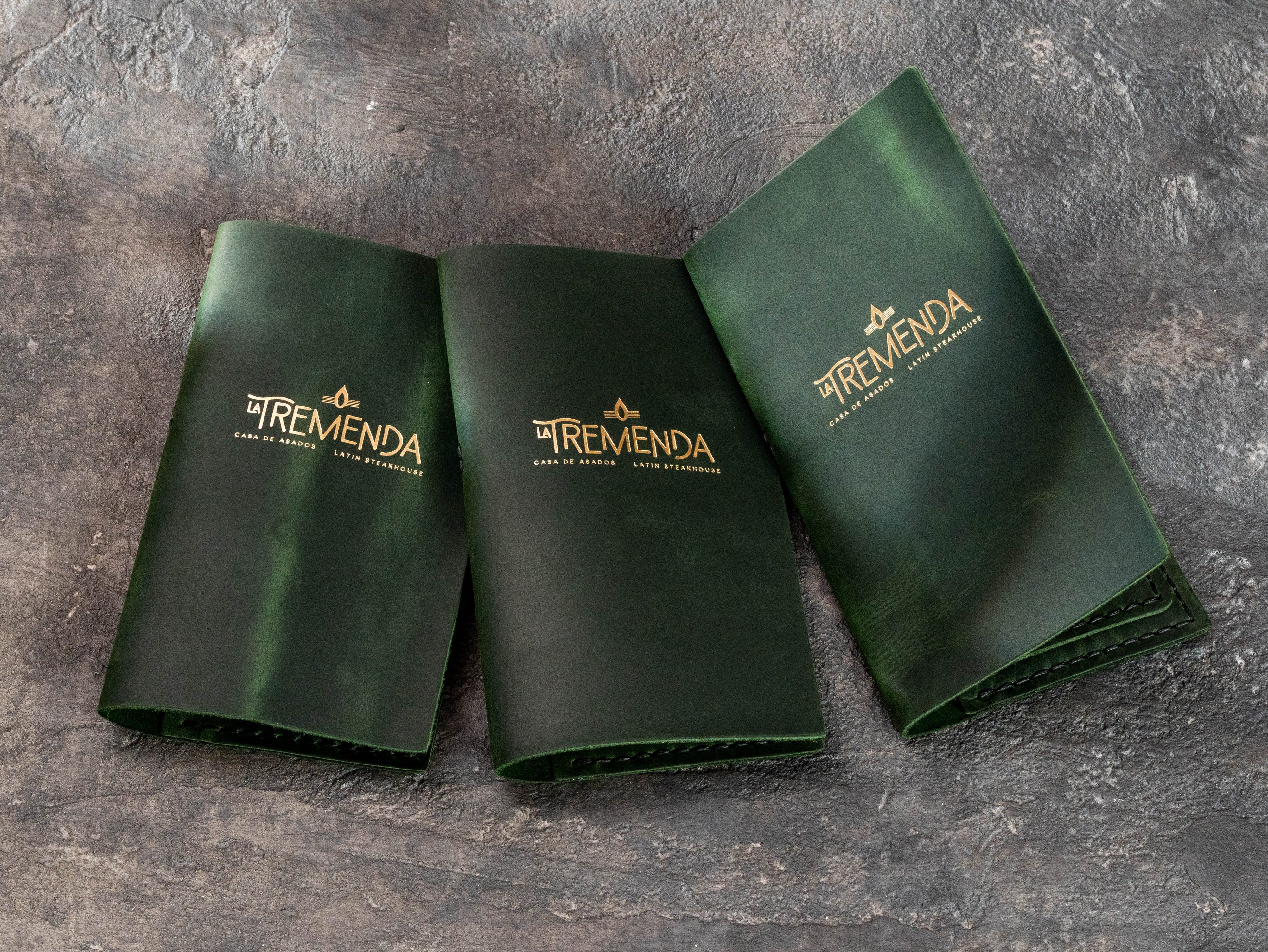 Dark green leather bill holders with gold restaurant logo for Latin steakhouse table service