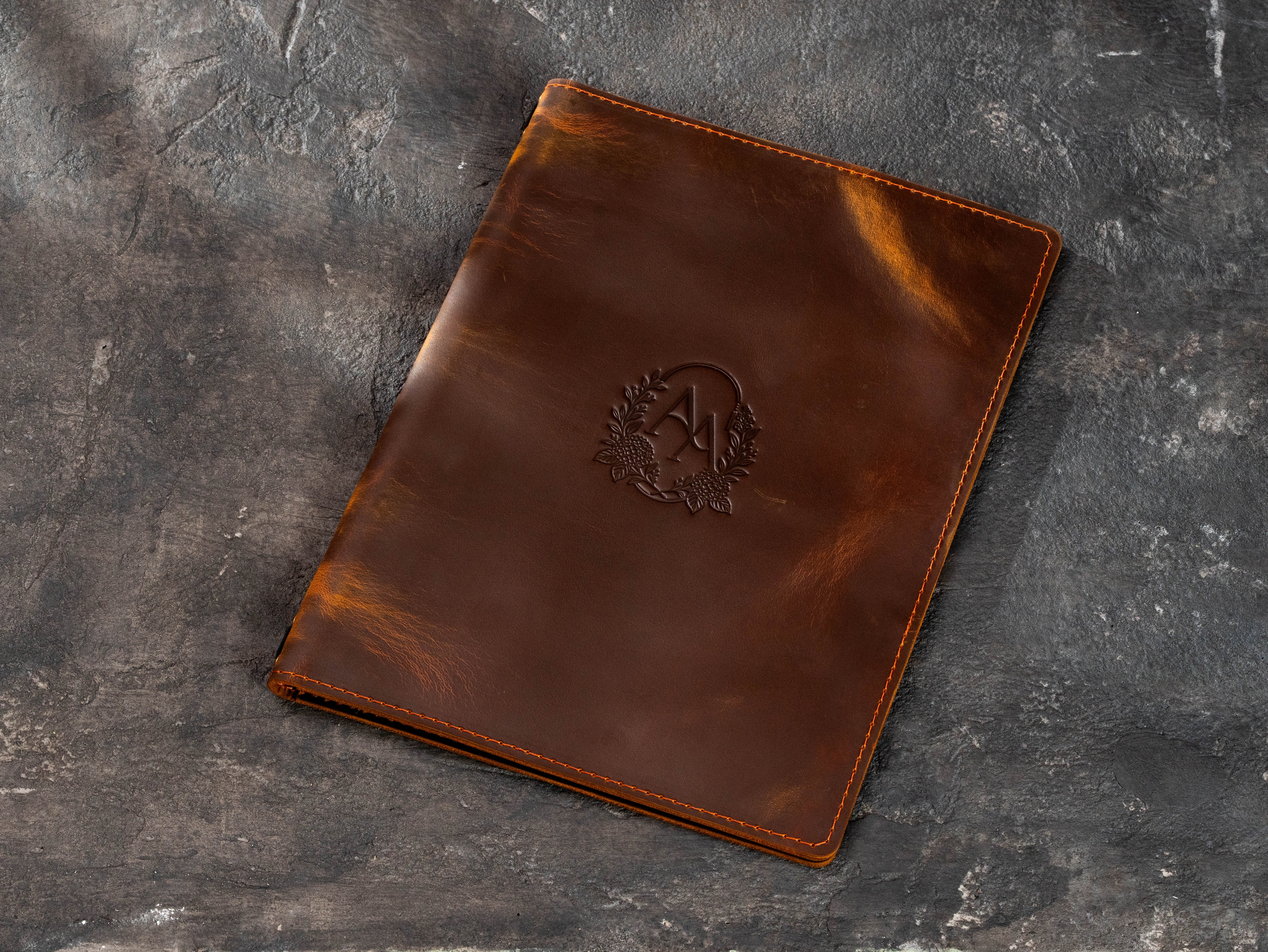 Personalized brown leather menu cover with custom initials inside a floral wreath design