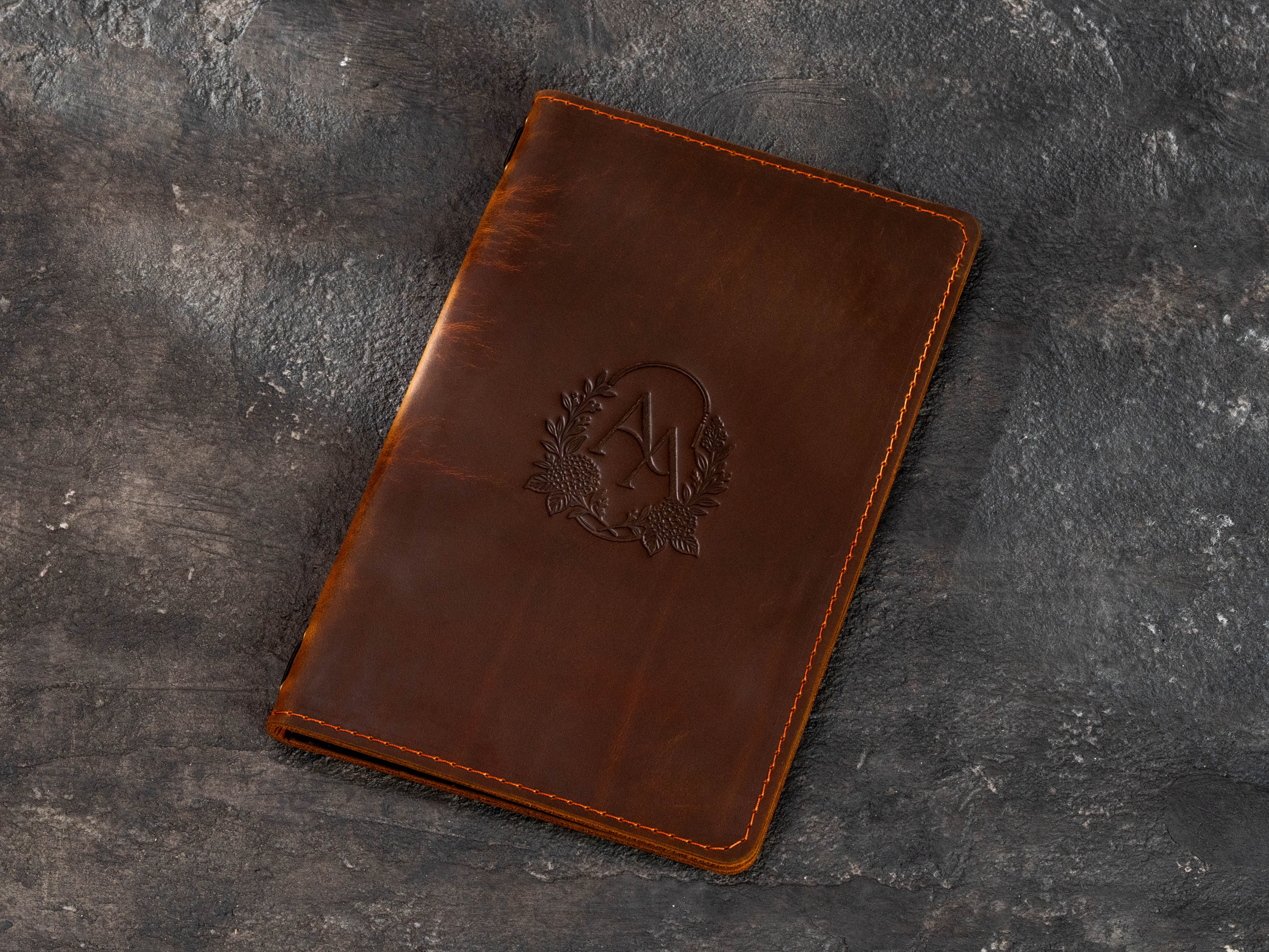 Brown leather menu covers with custom monogram and elastic cord binding for printed menu pages