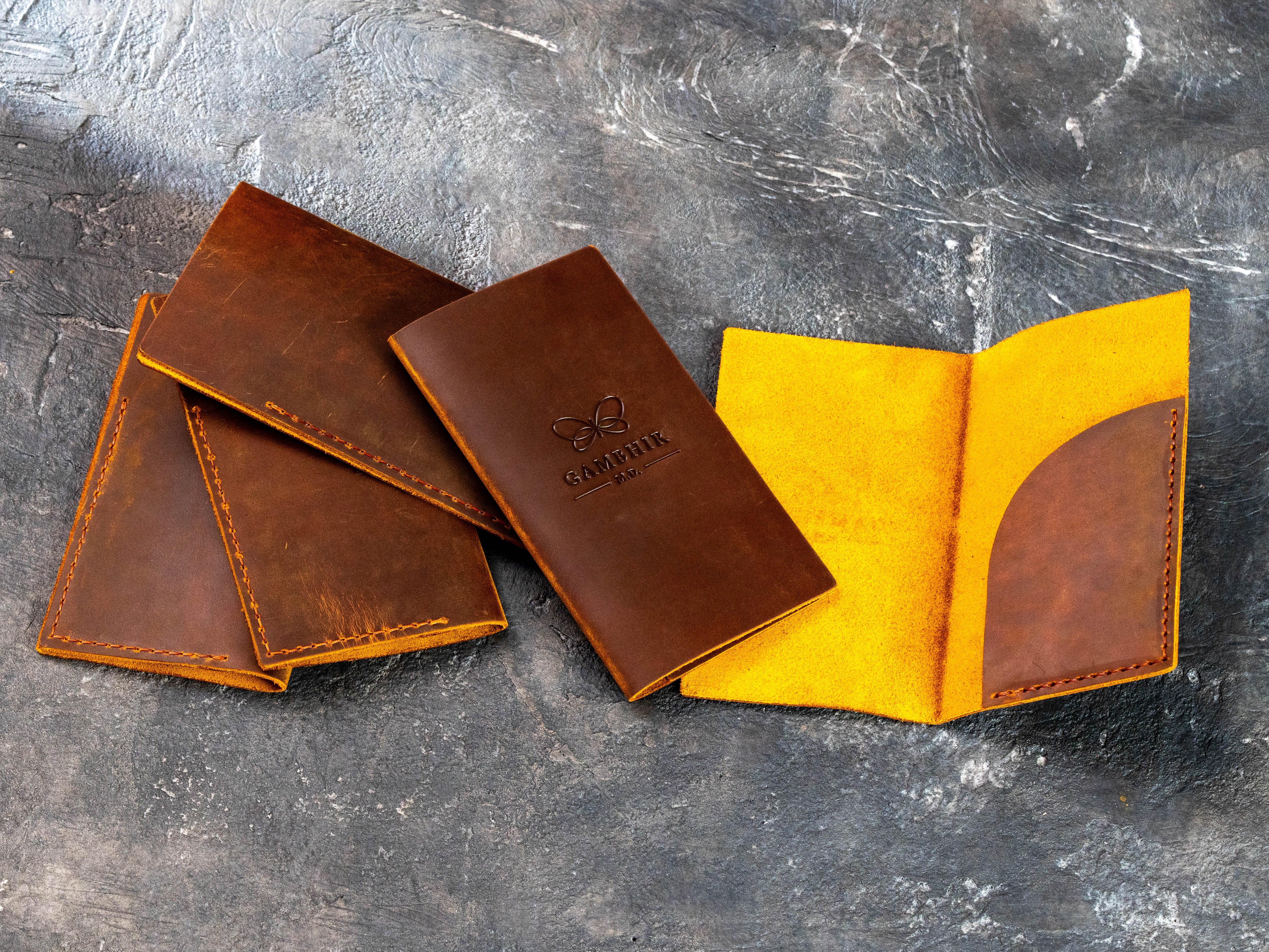 Open and closed chestnut leather bill holders with custom Gambhir M.D. branding and interior receipt pocket