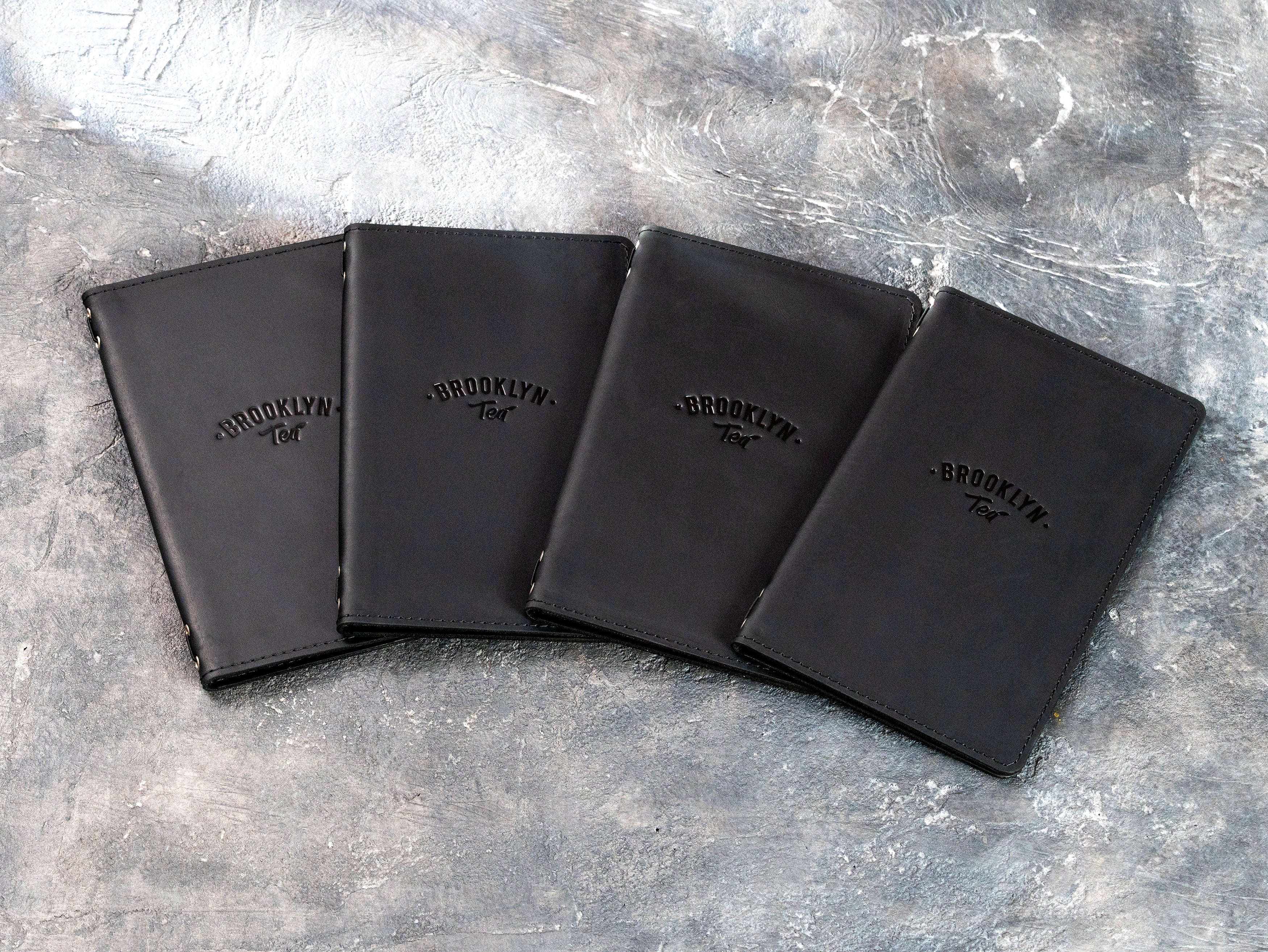 Back view of four black leather restaurant menu covers with clean stitched construction