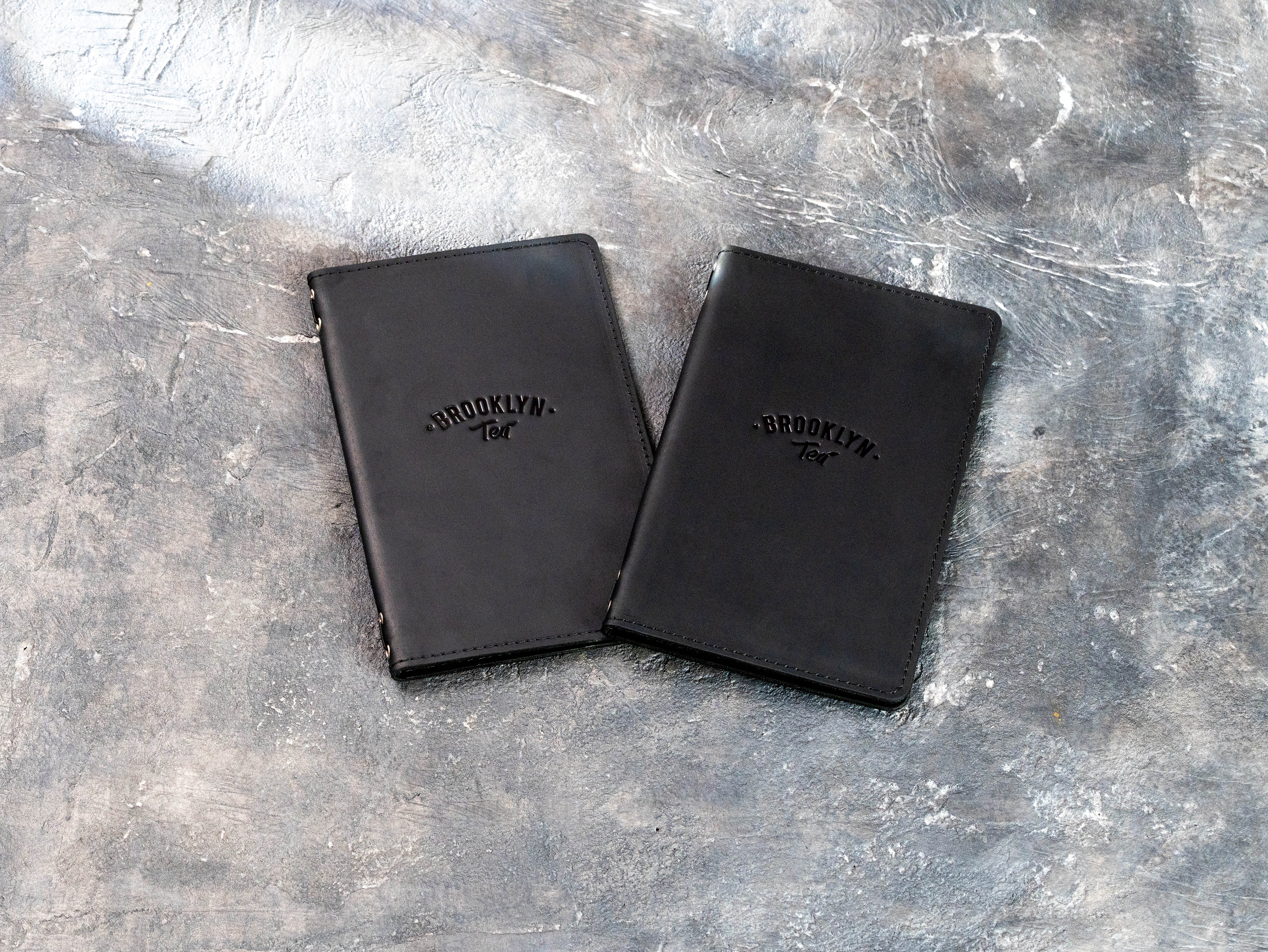Two personalized black leather menu covers with blind embossed restaurant branding and stitched edges