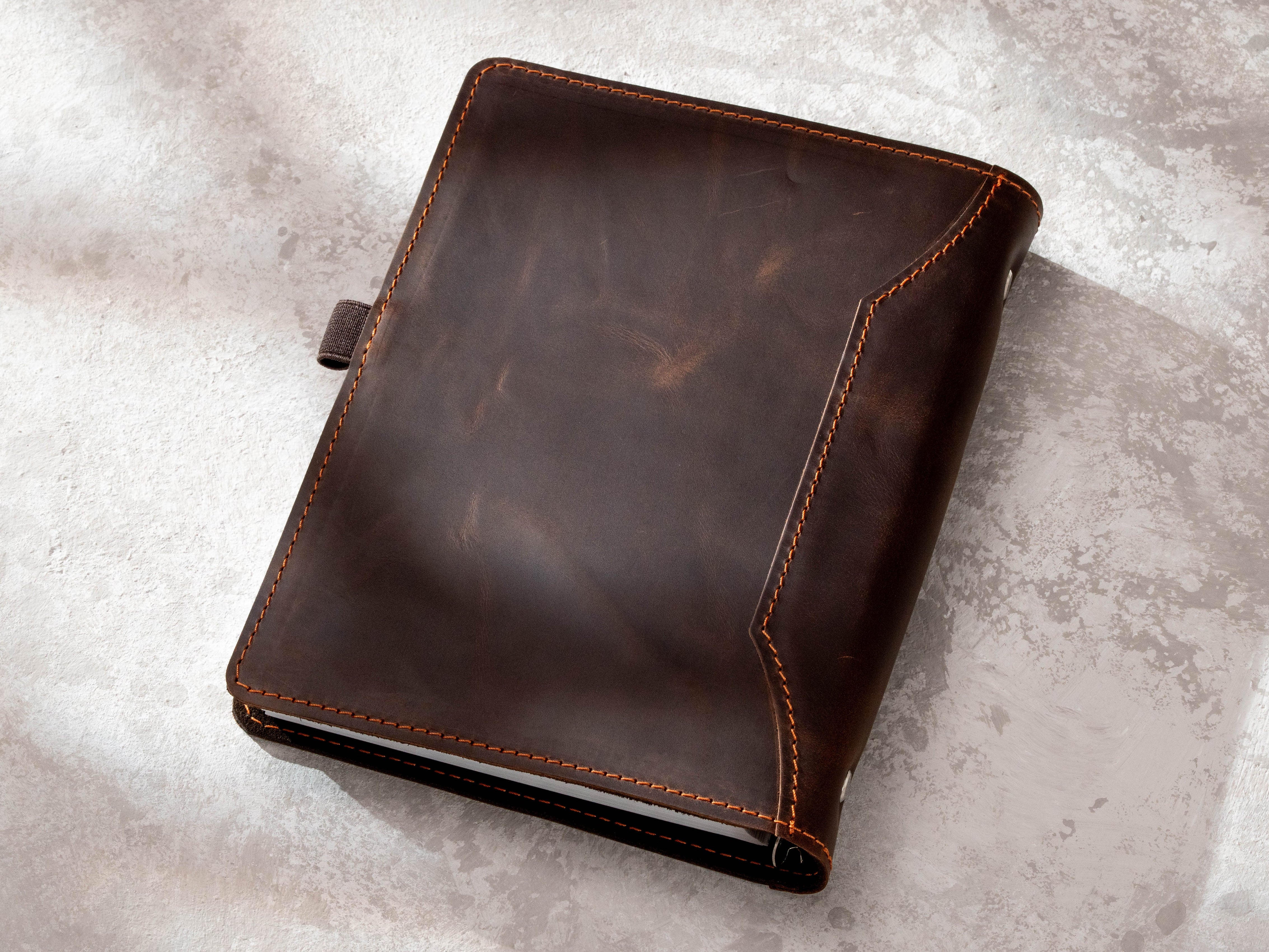 Back view of dark brown leather recipe binder with stitched edges and natural leather texture