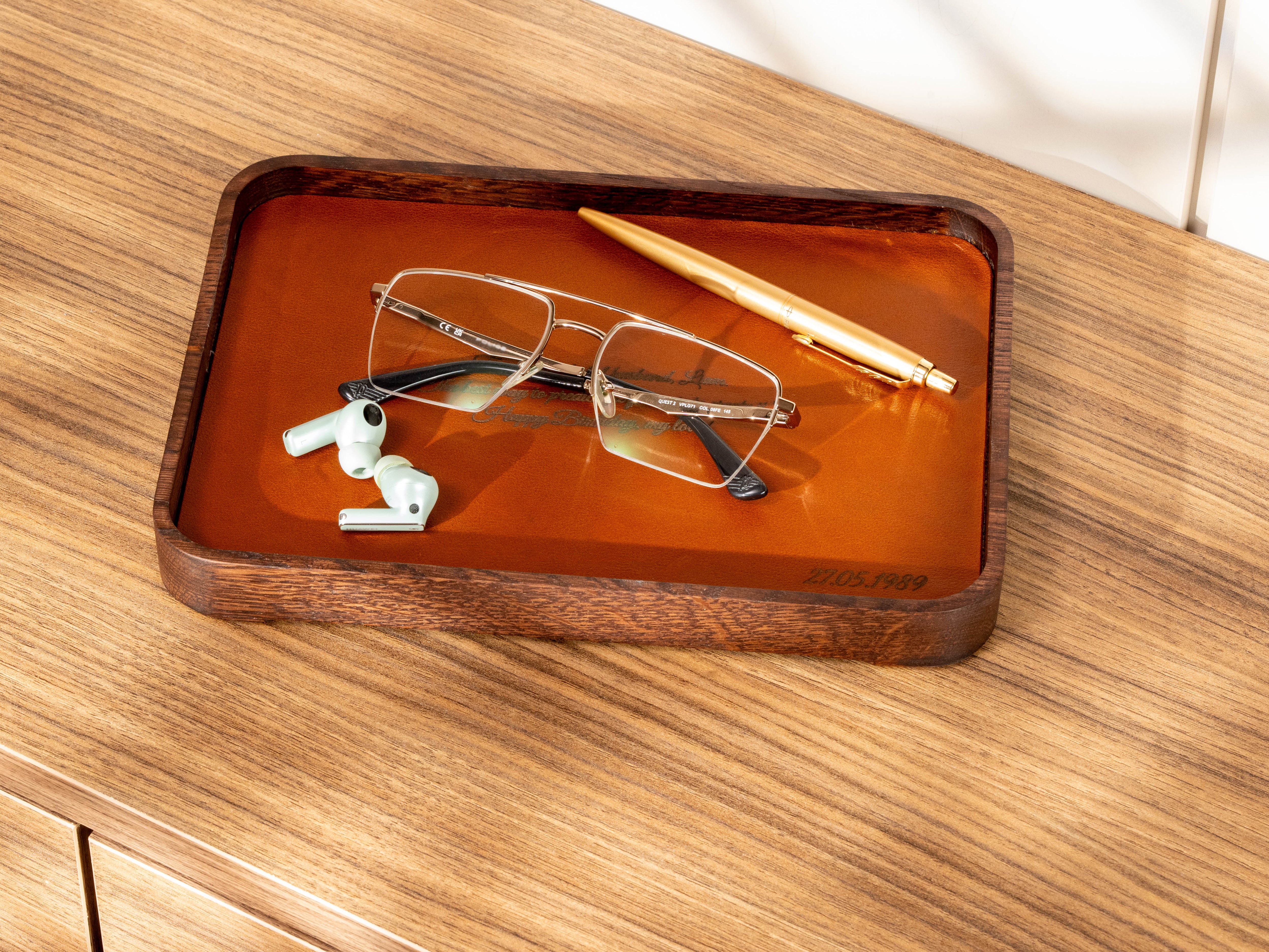 Personalized oak wood valet tray with Camel leather insert, custom engraved quote and date, holding glasses, earbuds and gold pen.