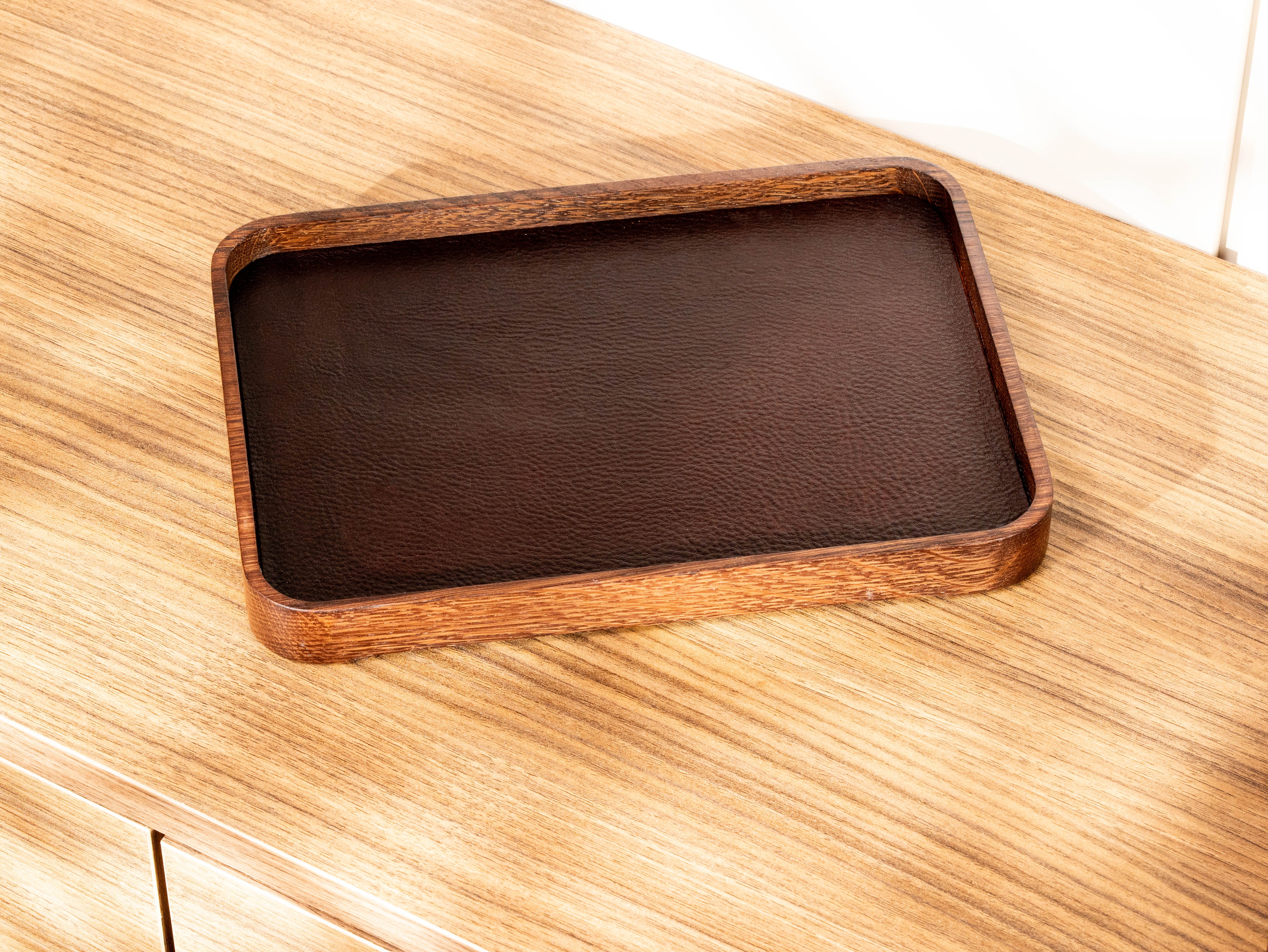 Dark oak wood catchall tray with dark brown top-grain leather insert and raised wooden edges.