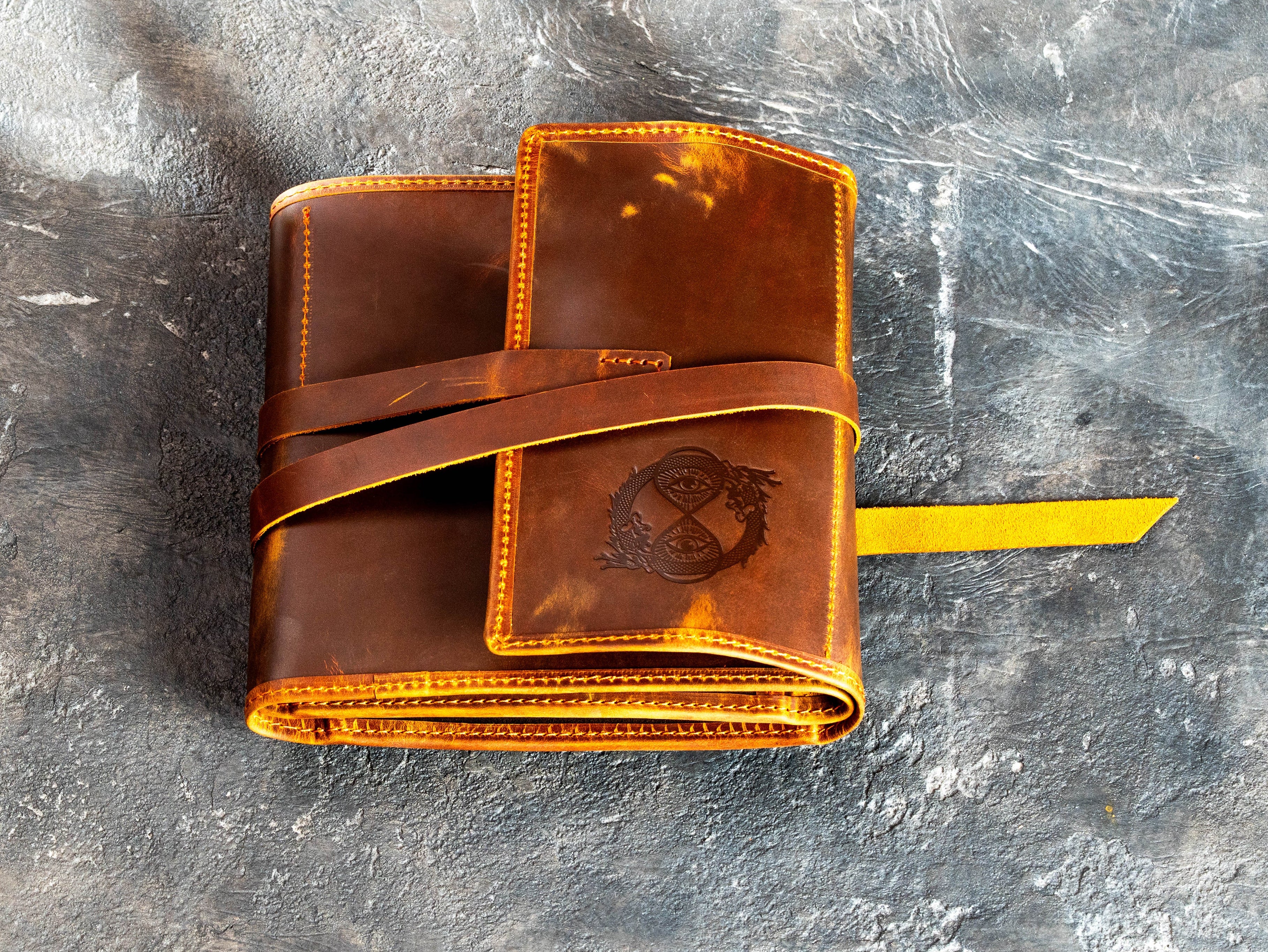 Closed waxed leather artist organizer with long wrap strap, personalized exterior design, and yellow suede accent