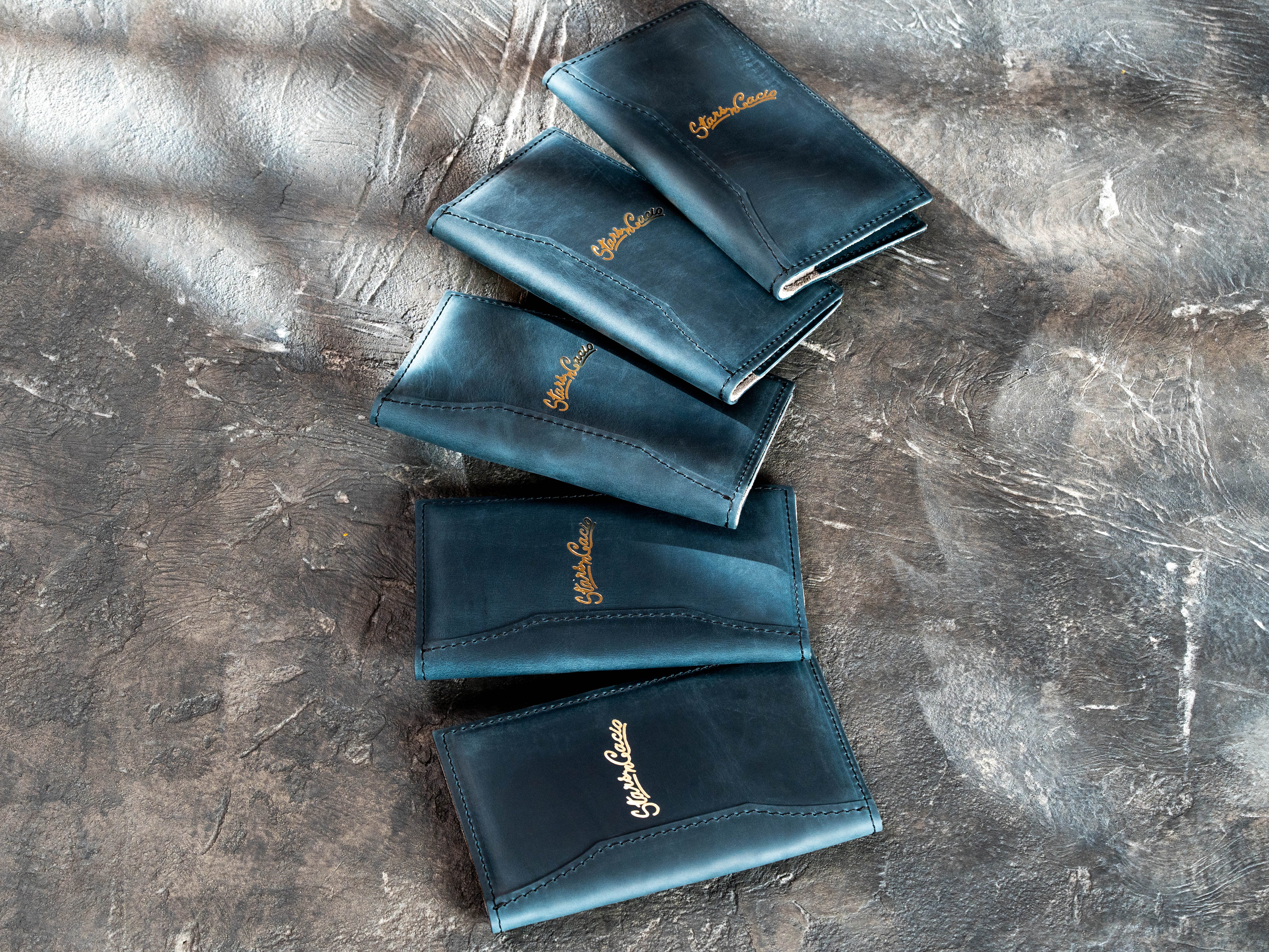 Stacked blue leather restaurant check presenters with gold foil business logos and stitched edges