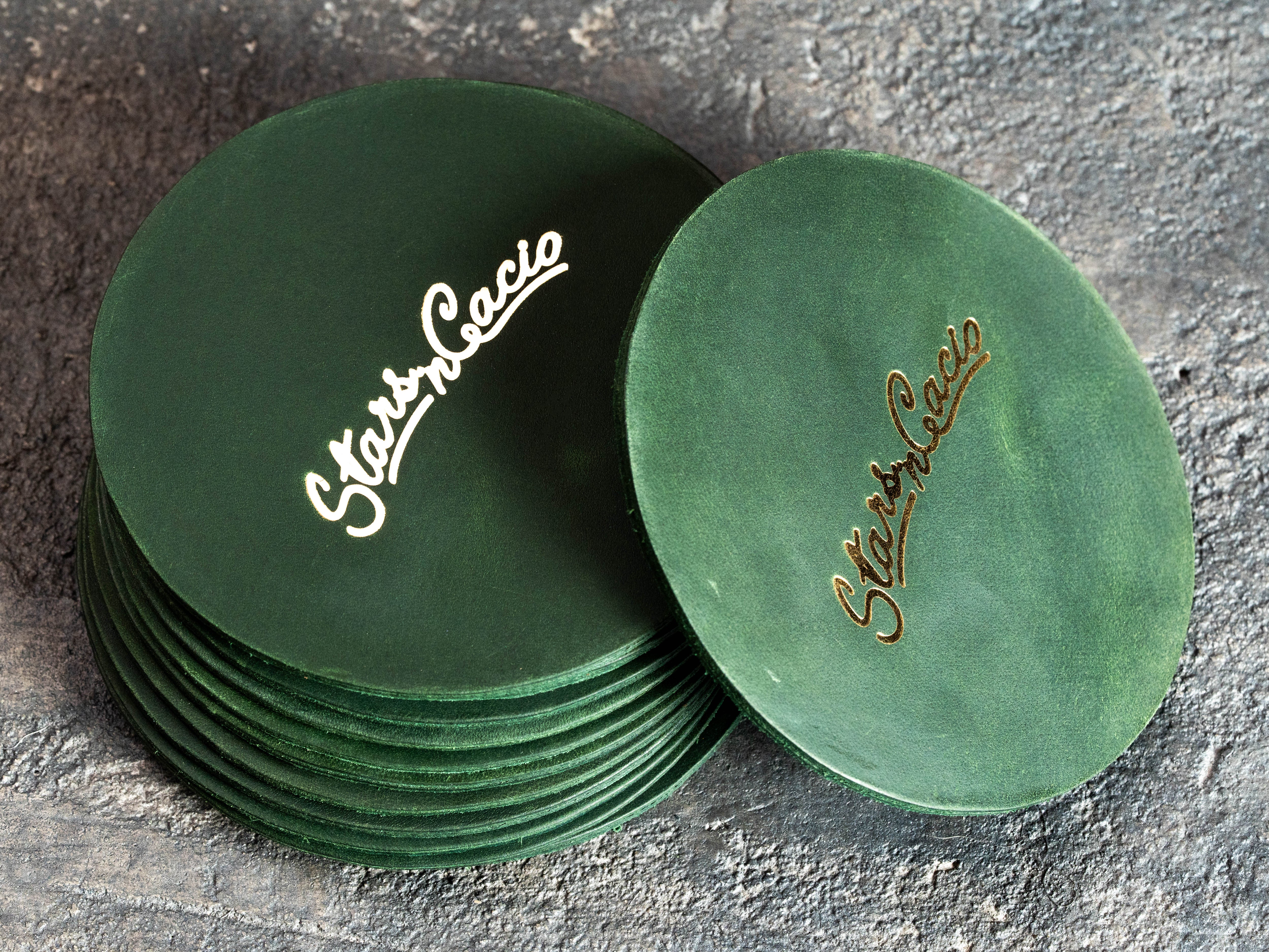Round green leather coasters with custom gold foil restaurant branding and natural waxed texture