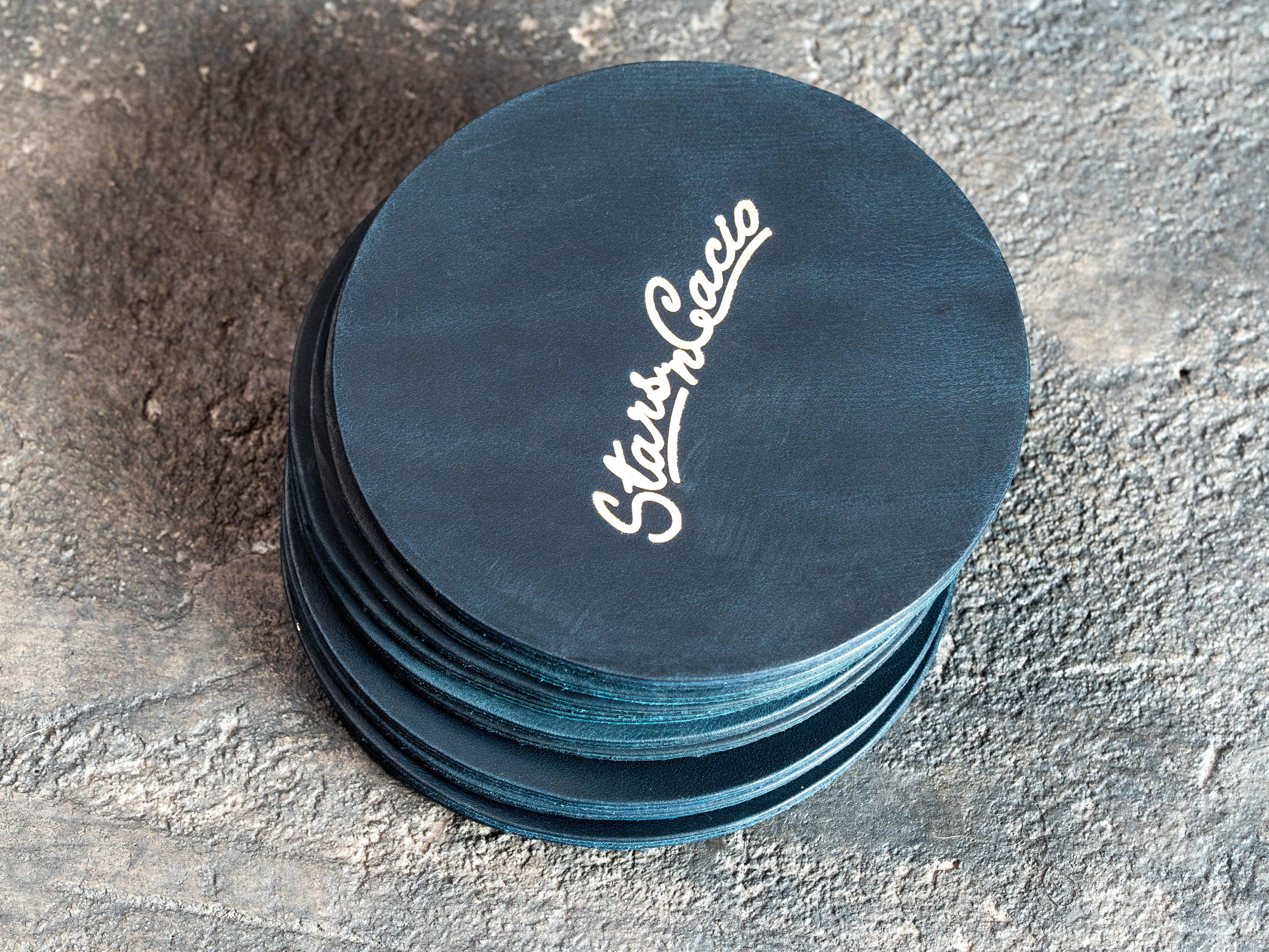 Stack of round blue leather coasters with custom gold foil restaurant branding