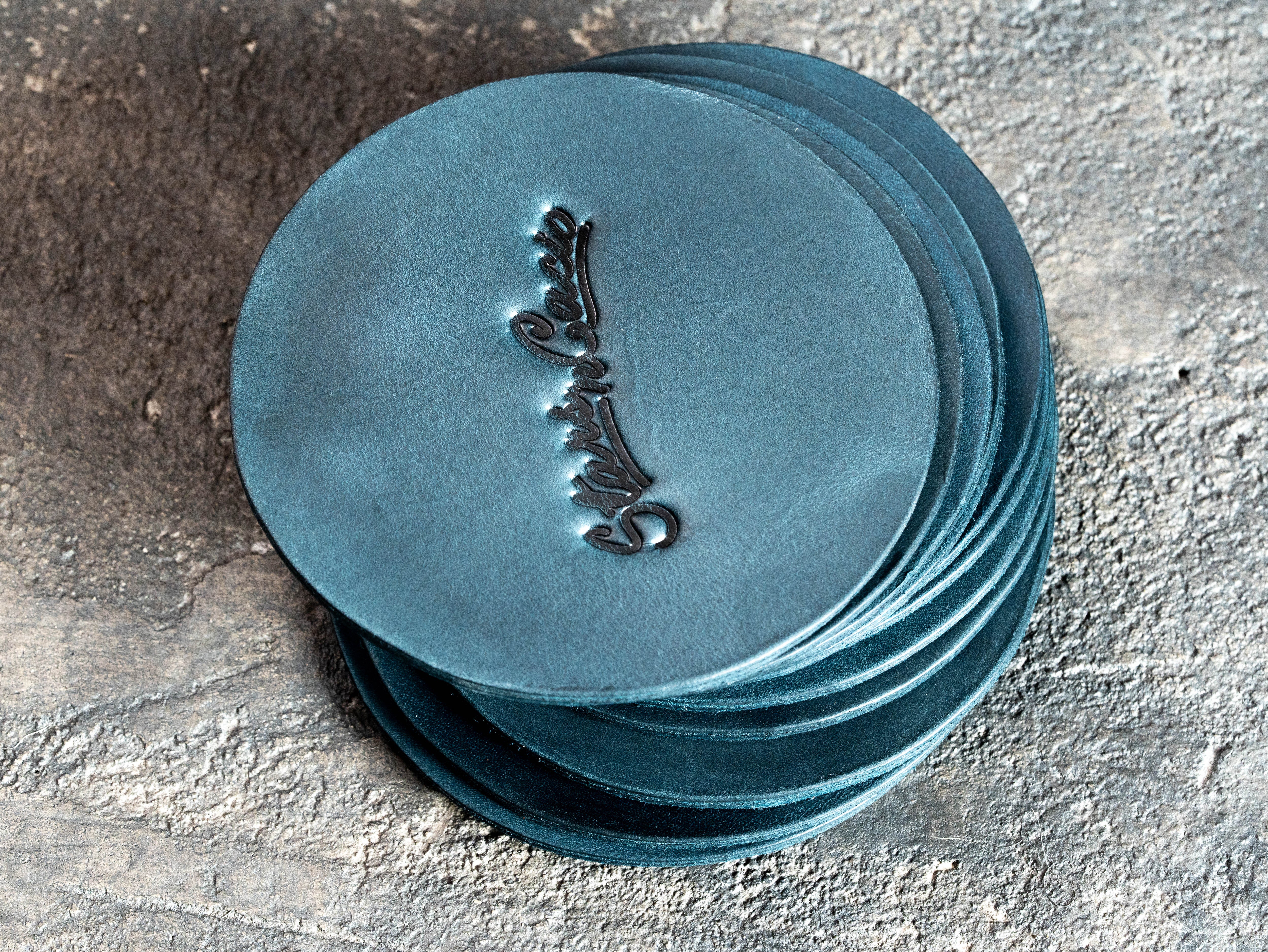 Stack of round blue leather coasters with deep blind embossed restaurant branding
