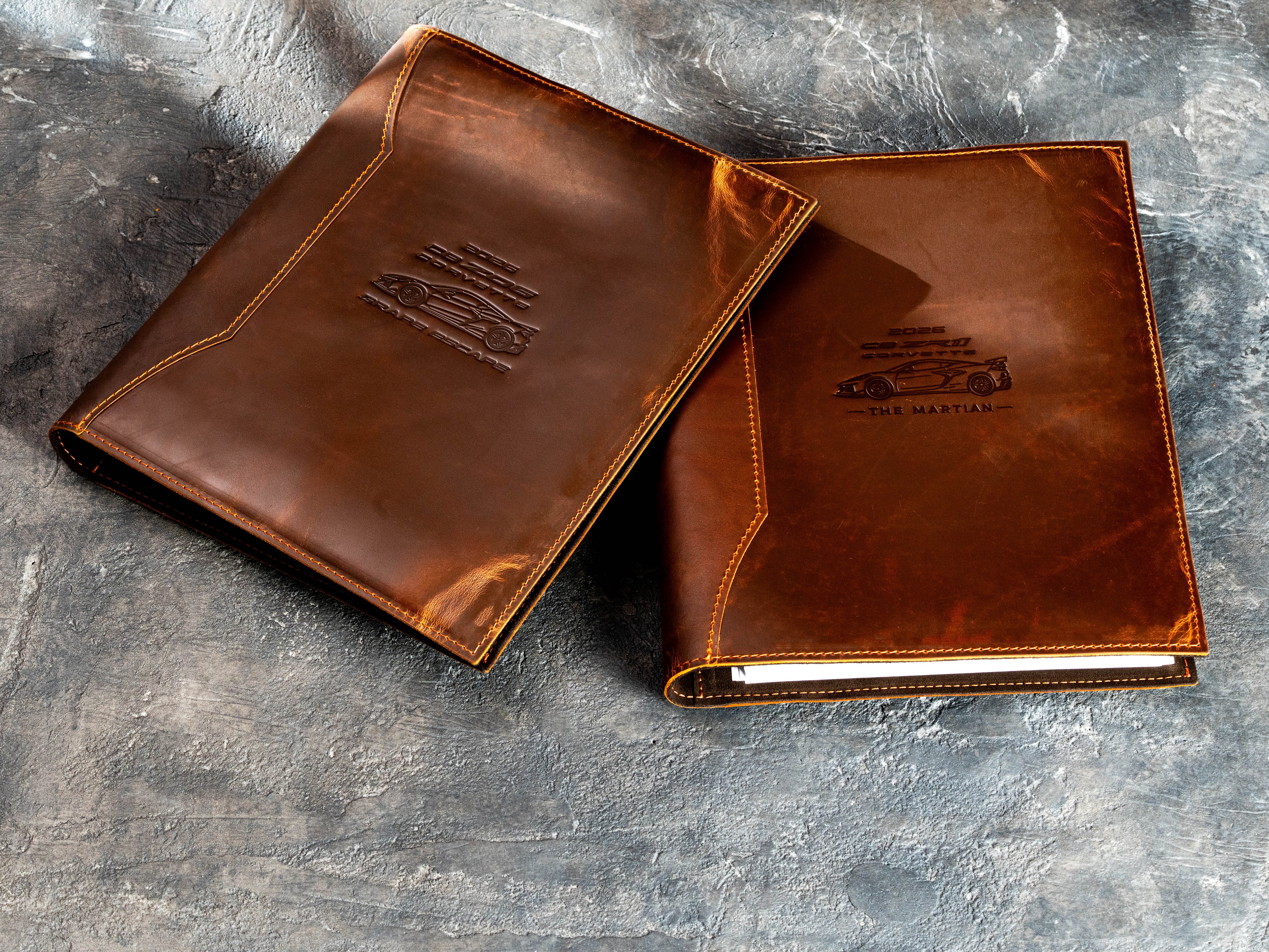 Two custom Chestnut leather vehicle document binders with personalized sports car designs and stitched edges