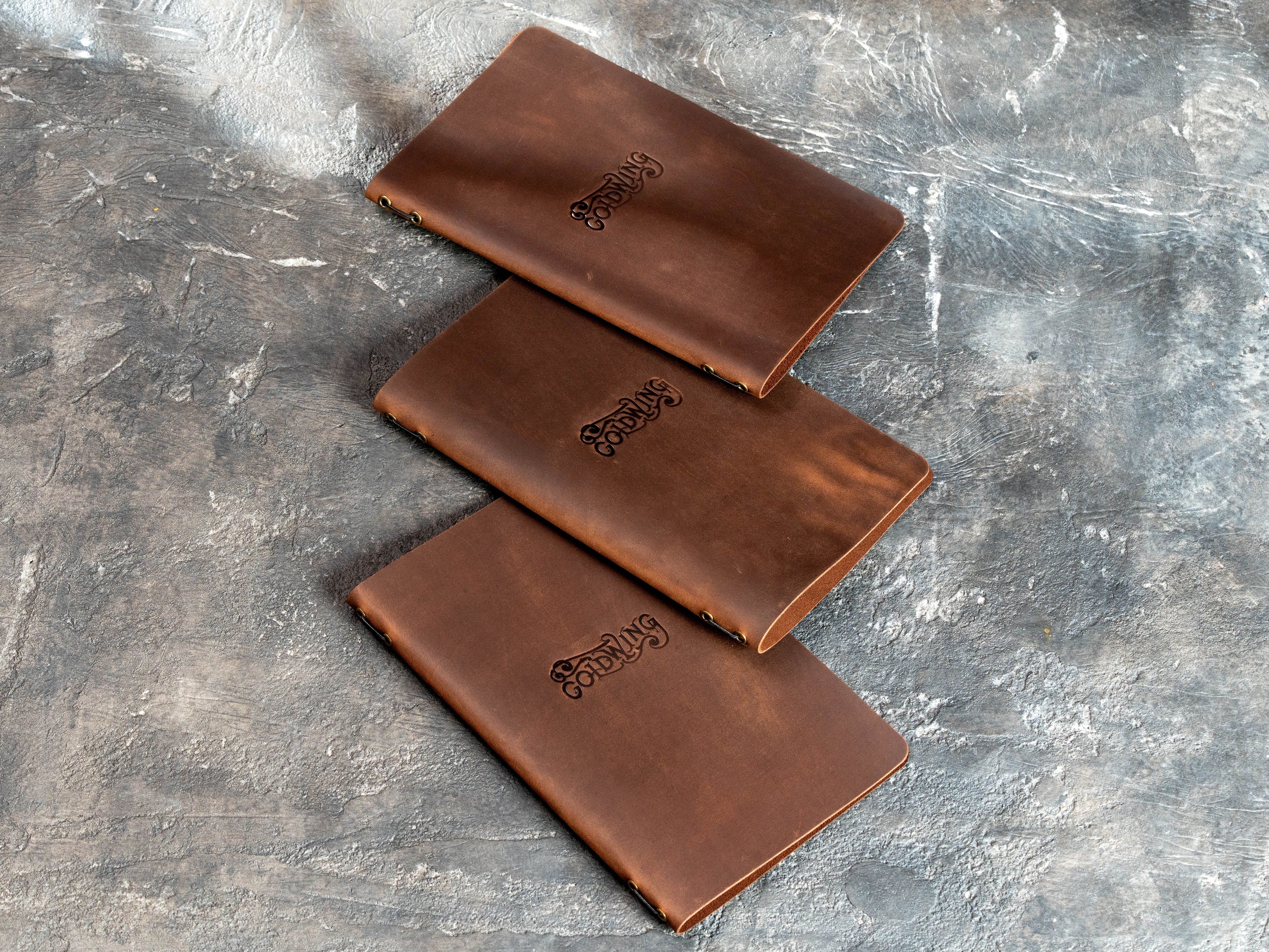 Three flexible brown leather bar menu covers with blind embossed logos and metal eyelets