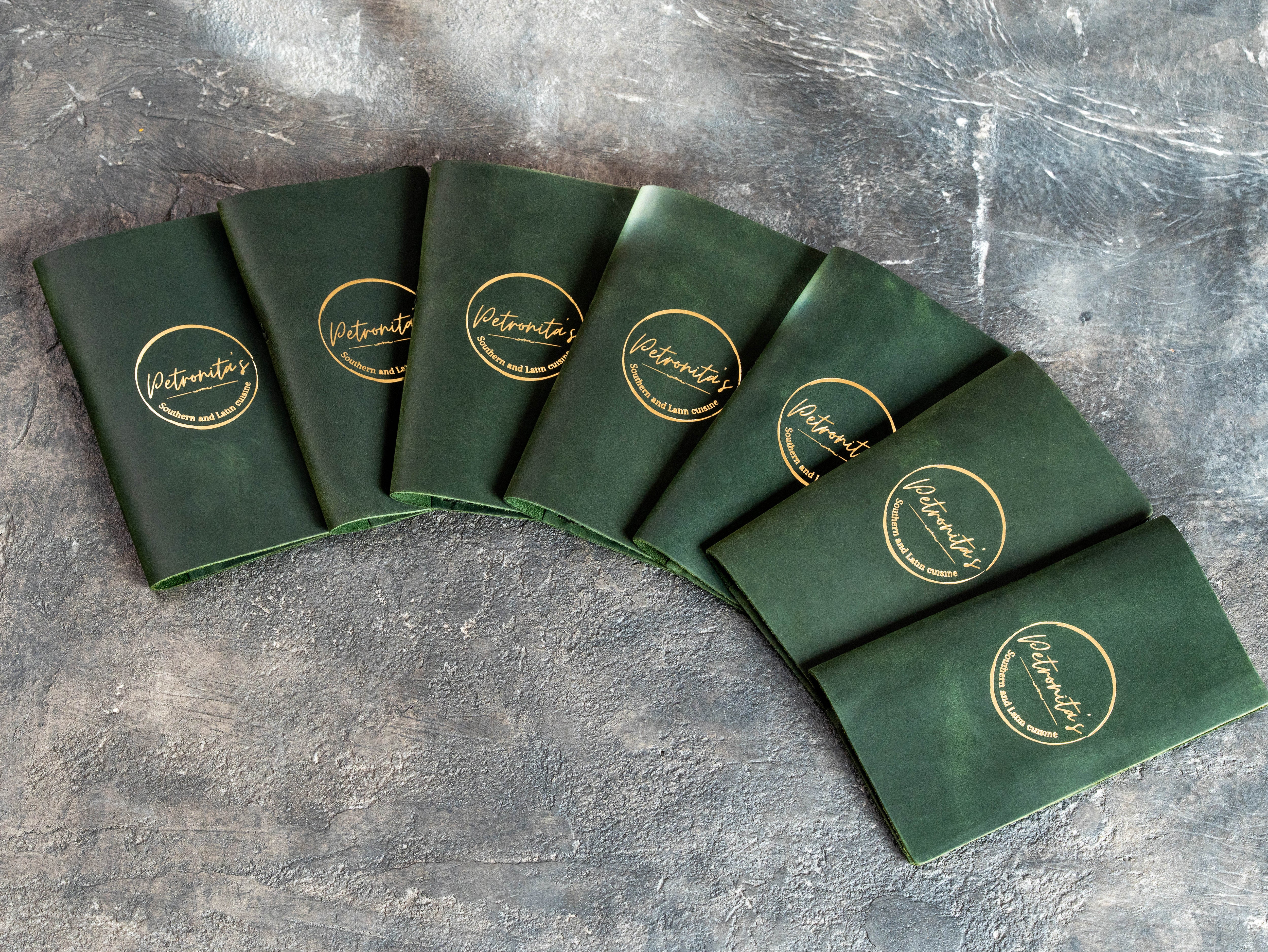 Set of custom green Crazy Horse leather check presenters with gold foil Petronita’s restaurant logos