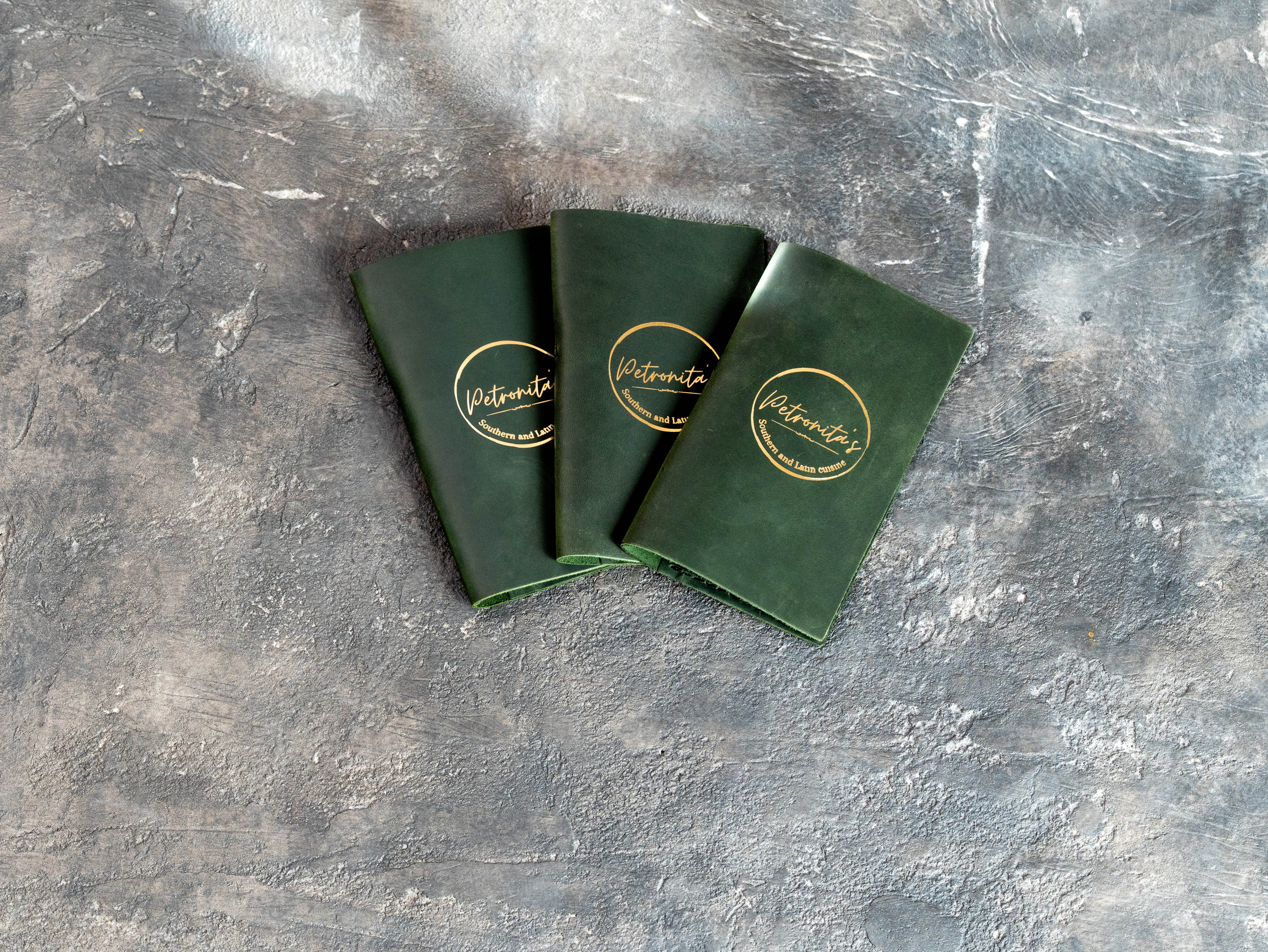 Three green leather restaurant bill holders with custom gold foil branding