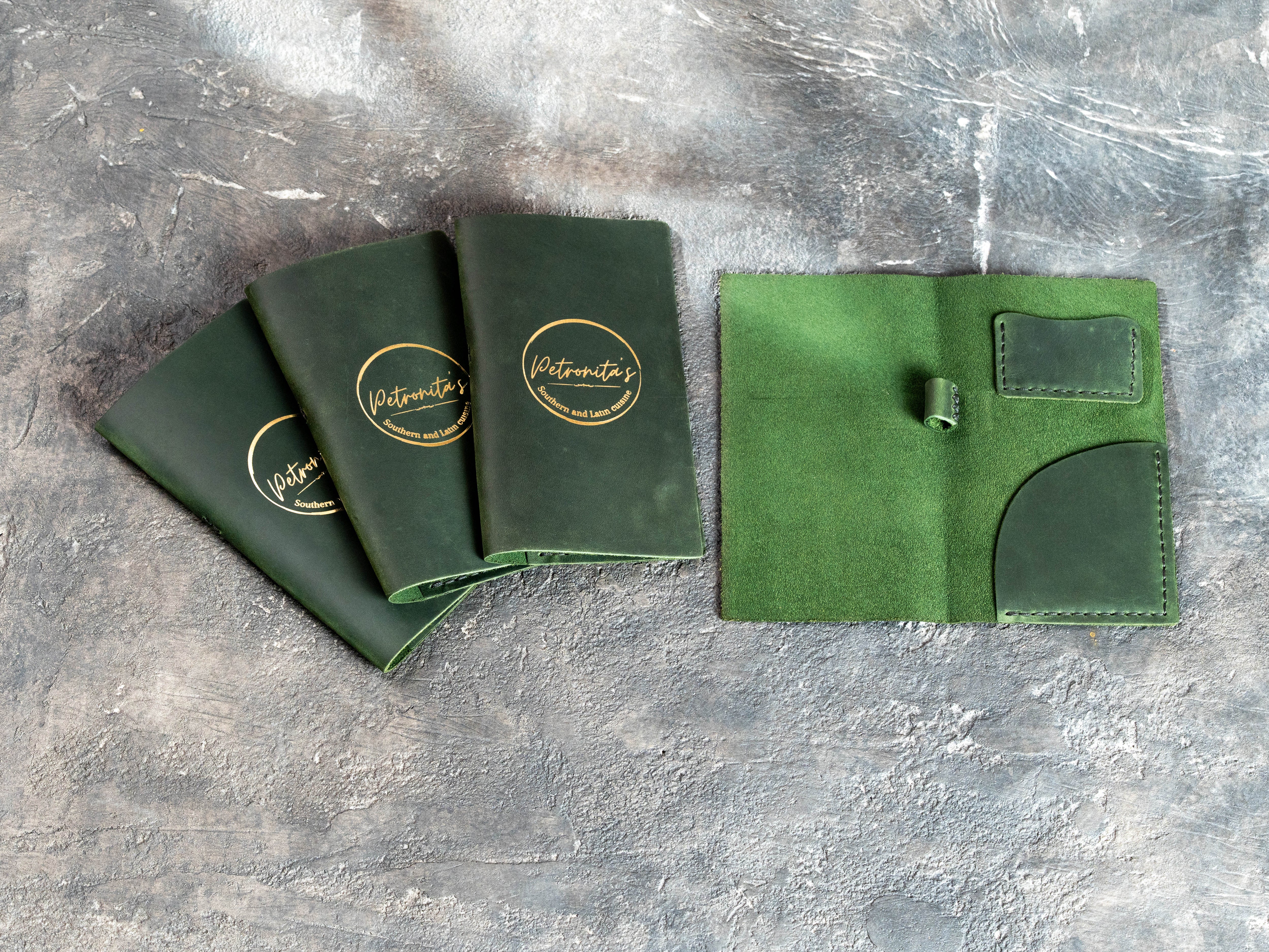 Custom green restaurant check presenters with gold foil logos and functional interior pockets