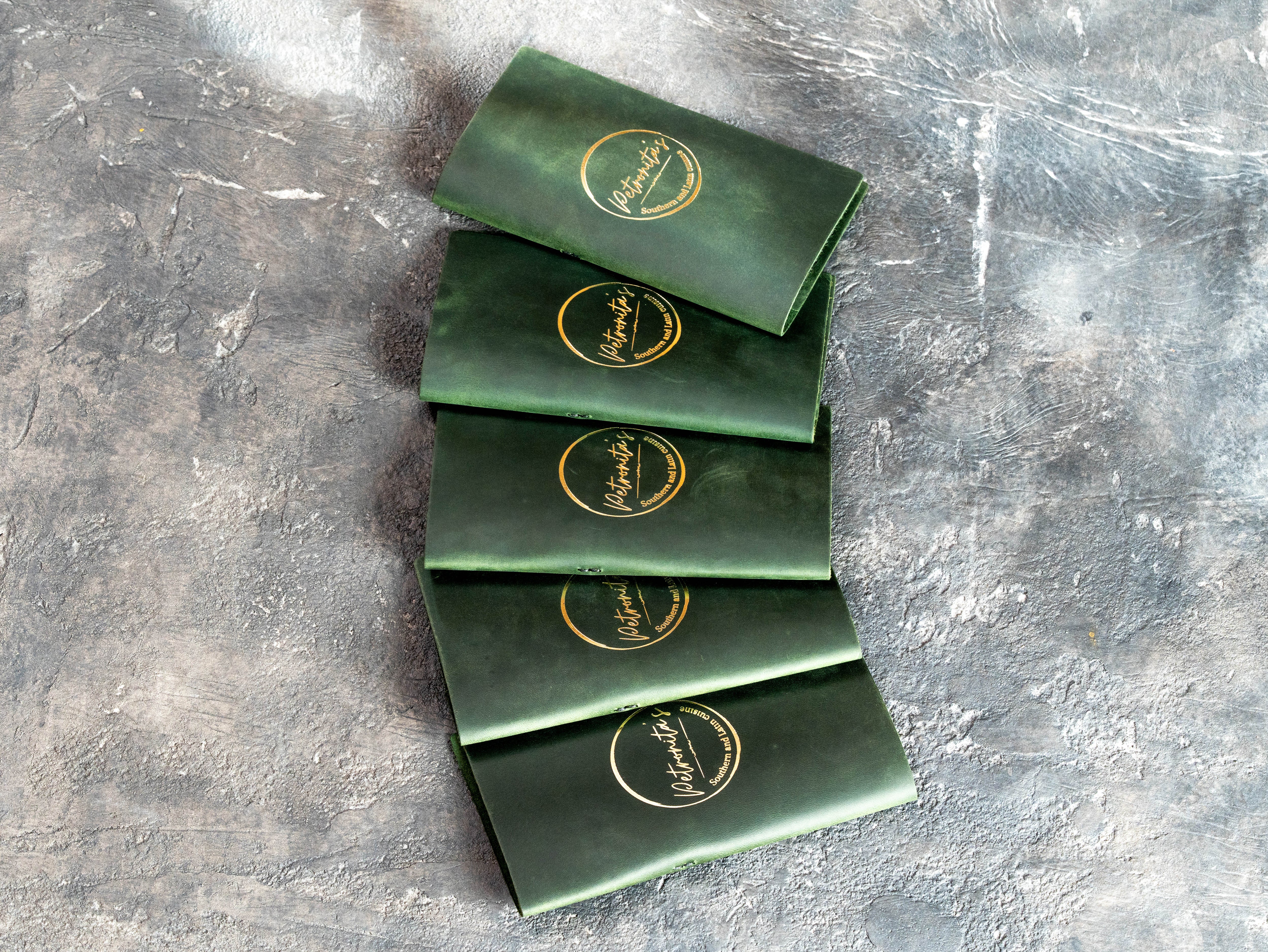Stack of green Crazy Horse leather check presenters with metallic gold restaurant logos