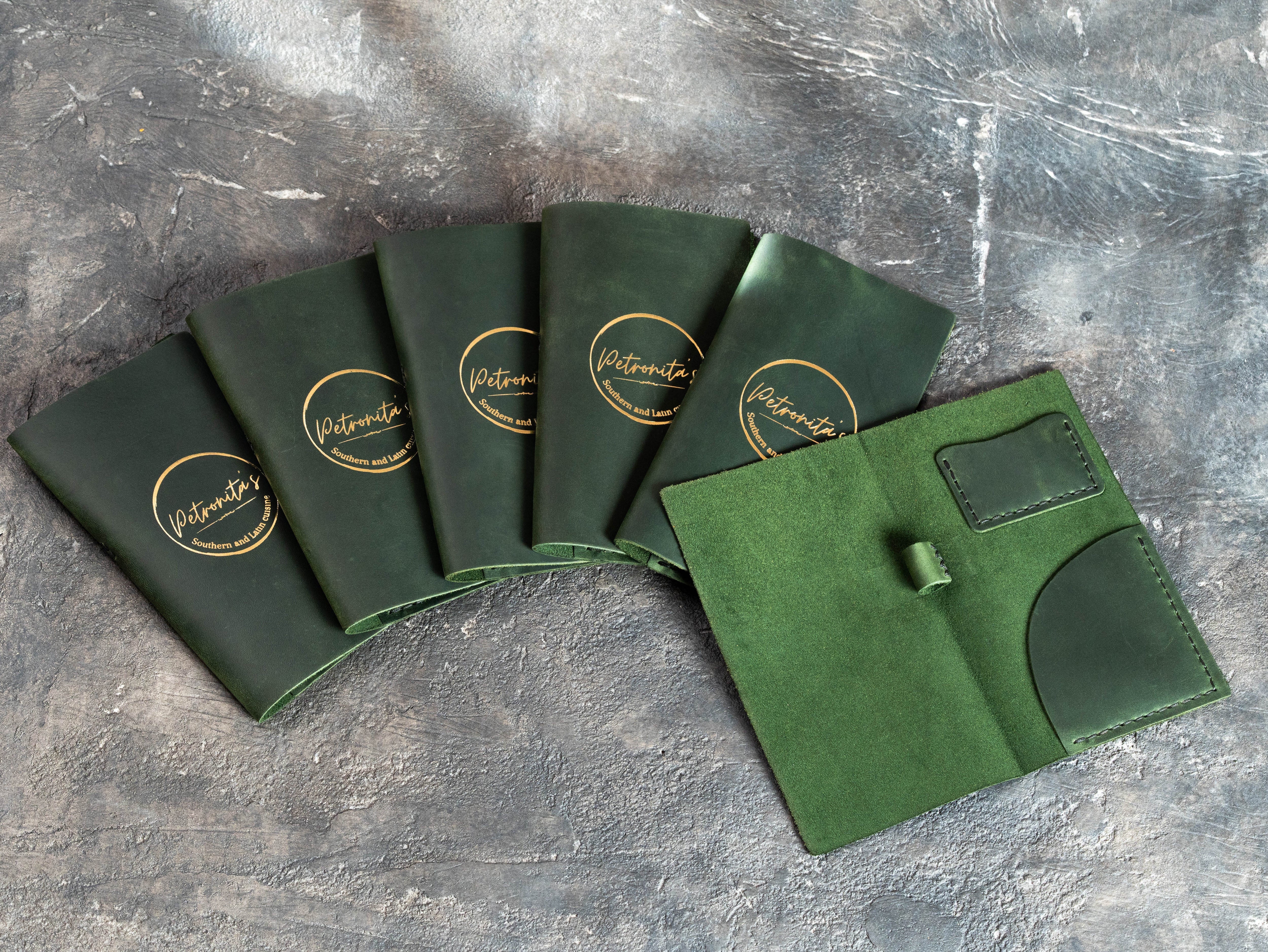 Bulk order of green leather bill presenters with gold foil Petronita’s branding and open interior design