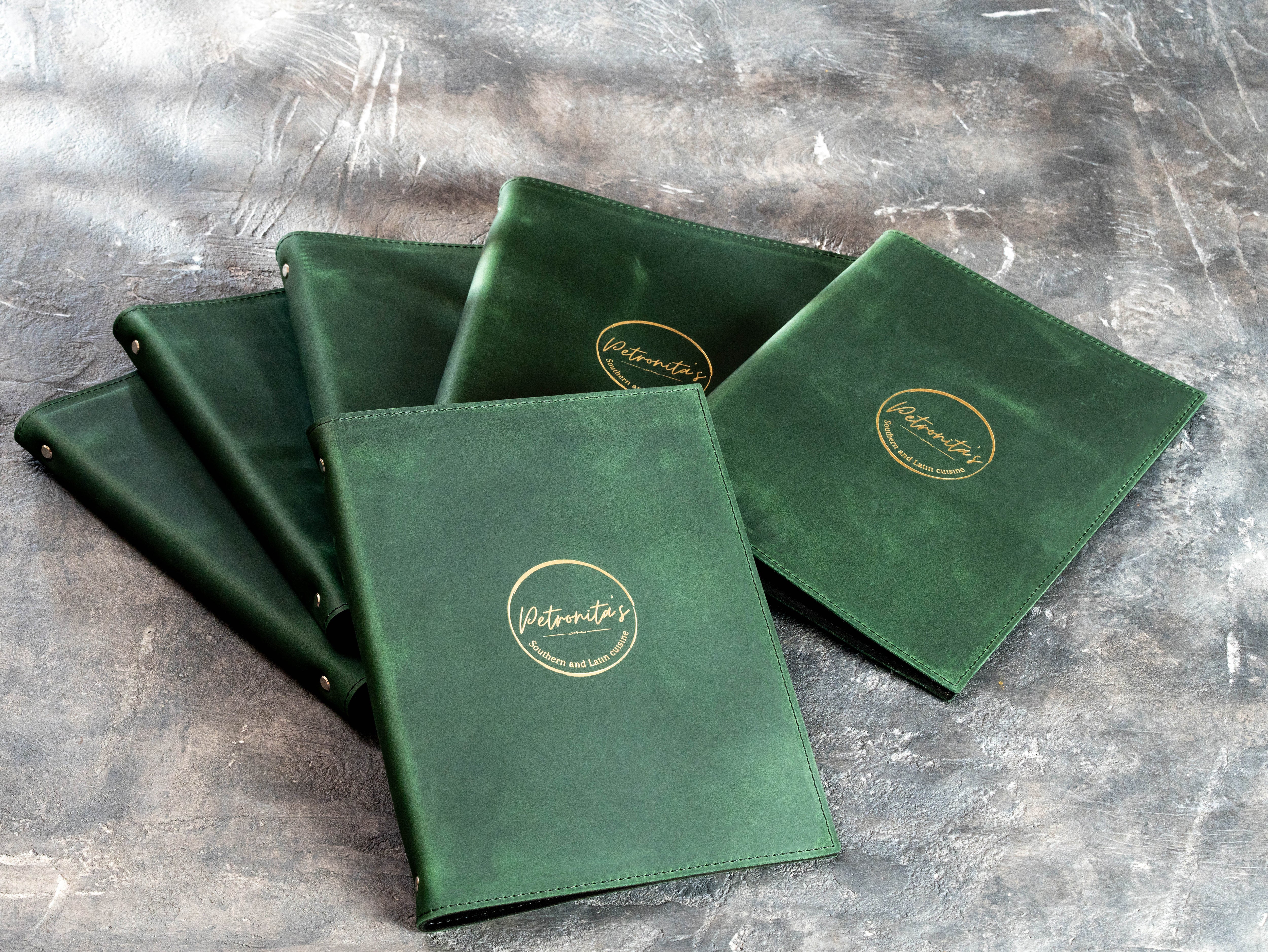 Multiple custom restaurant binders in green leather prepared for a bulk hospitality order