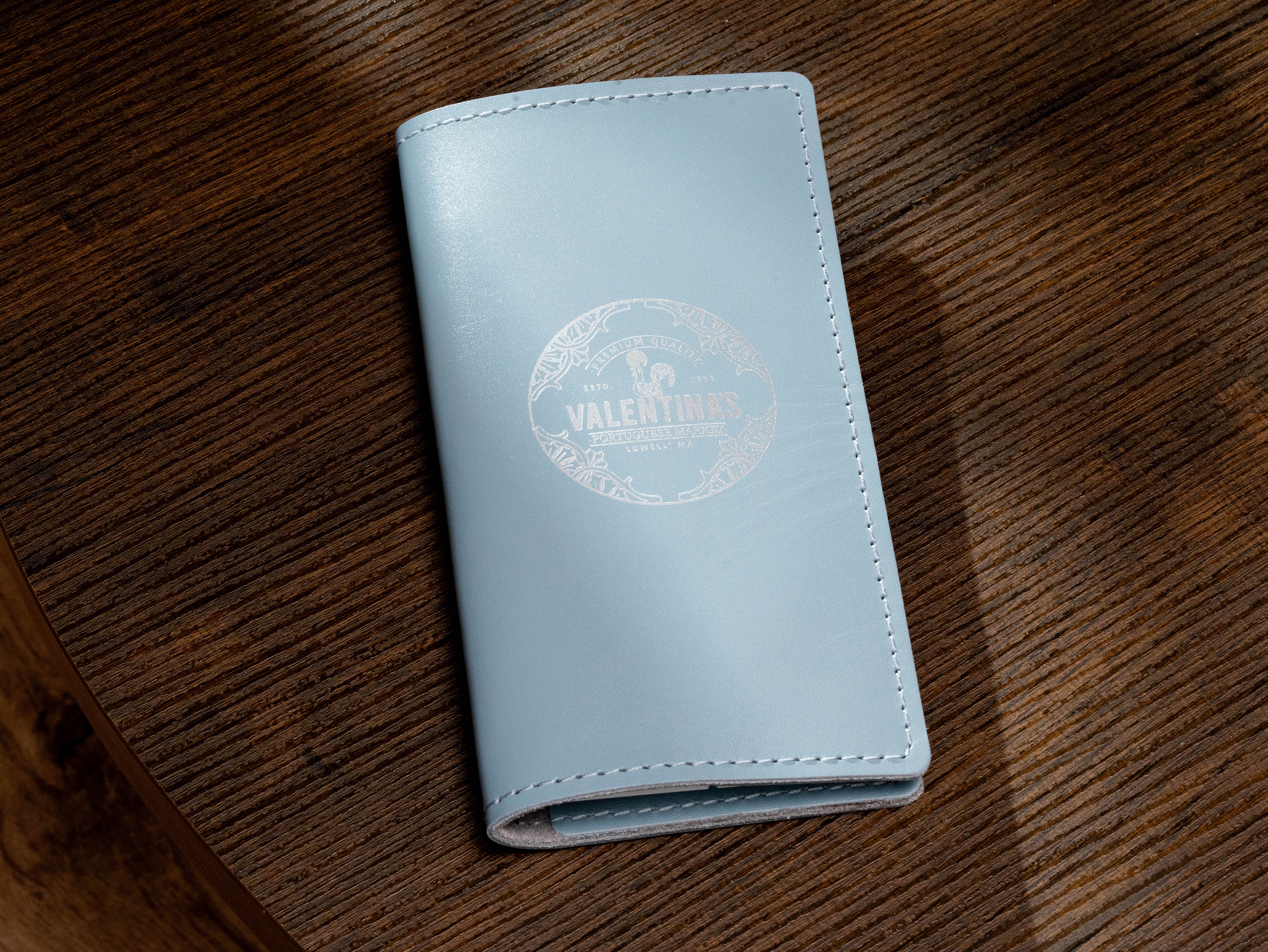 Custom ice blue leather check presenter with white Valentina’s Portuguese Market logo and stitched edges