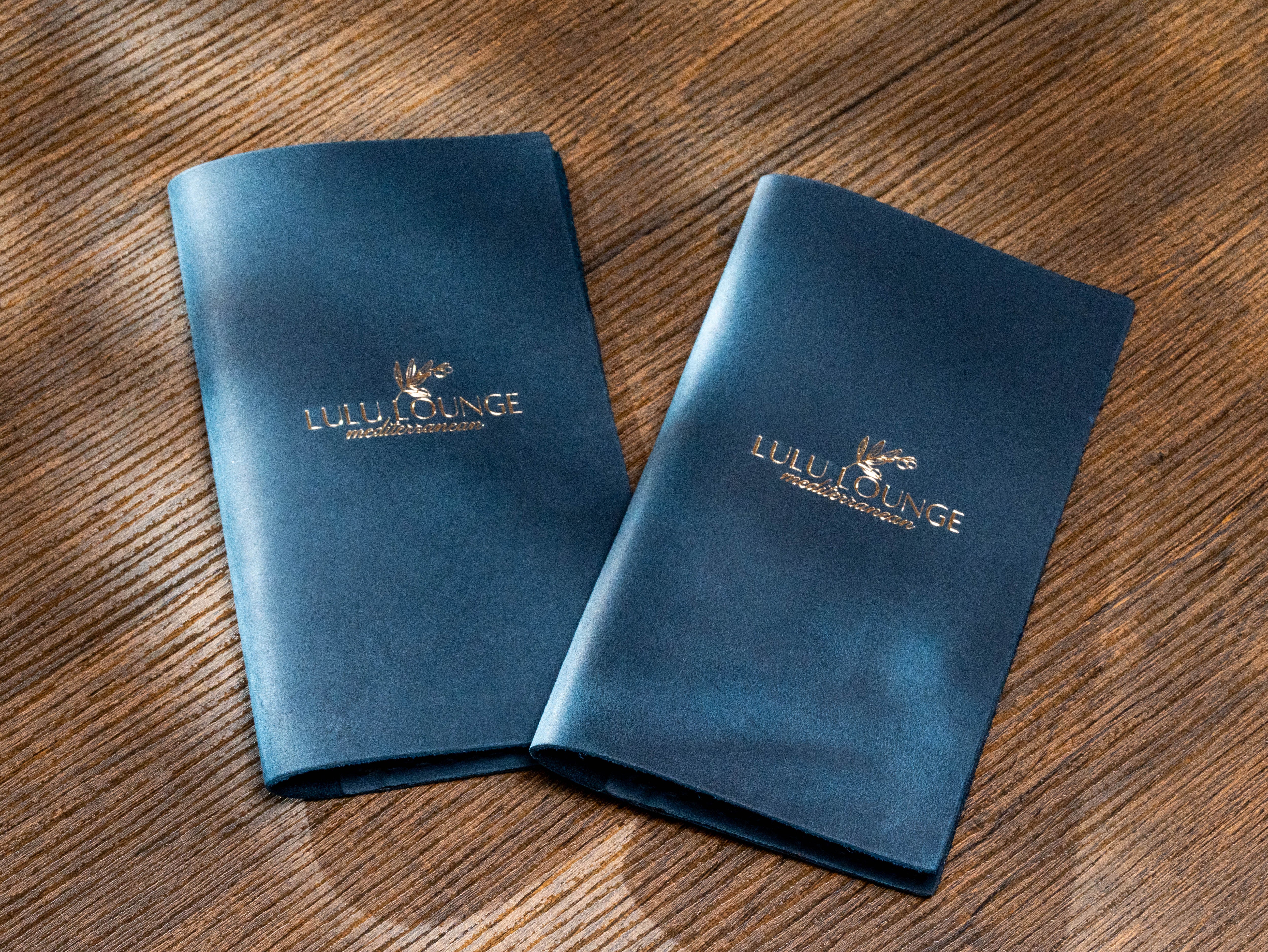 Two custom navy leather check presenters with gold Lulu Lounge Mediterranean logo for restaurant and lounge service