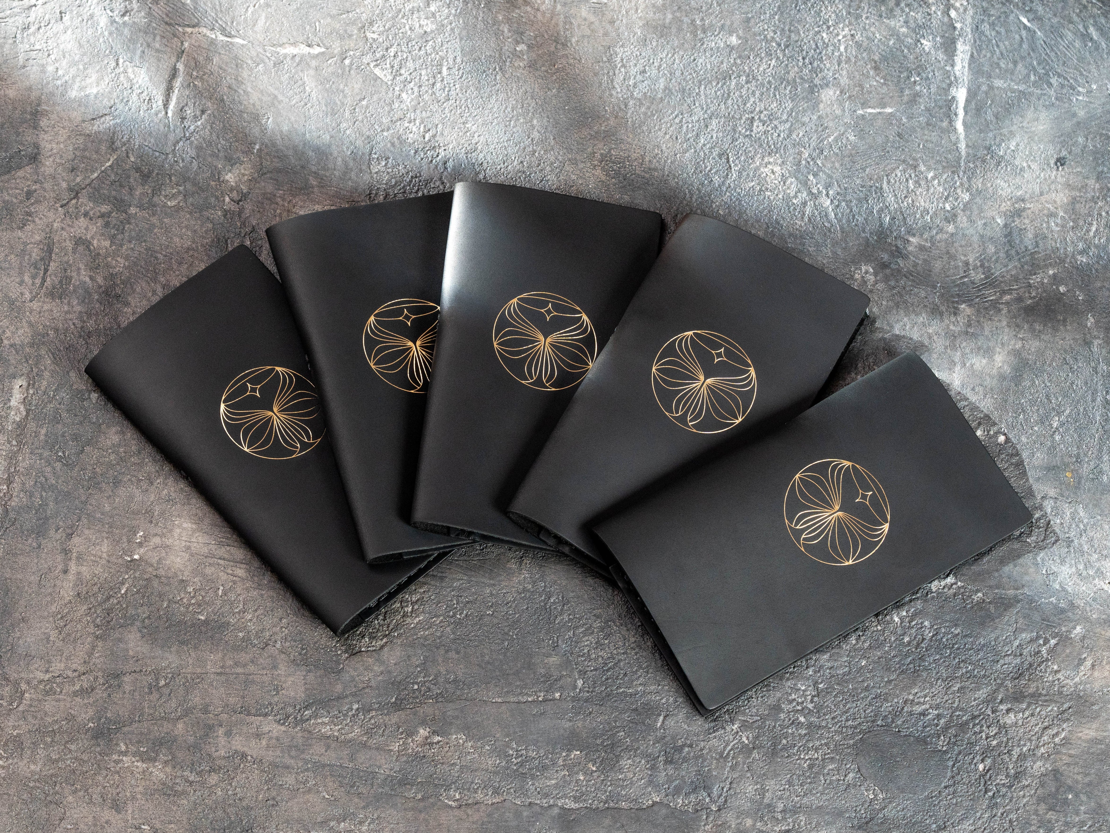 Five custom black leather check presenters with gold foil logos arranged in a fan-shaped display