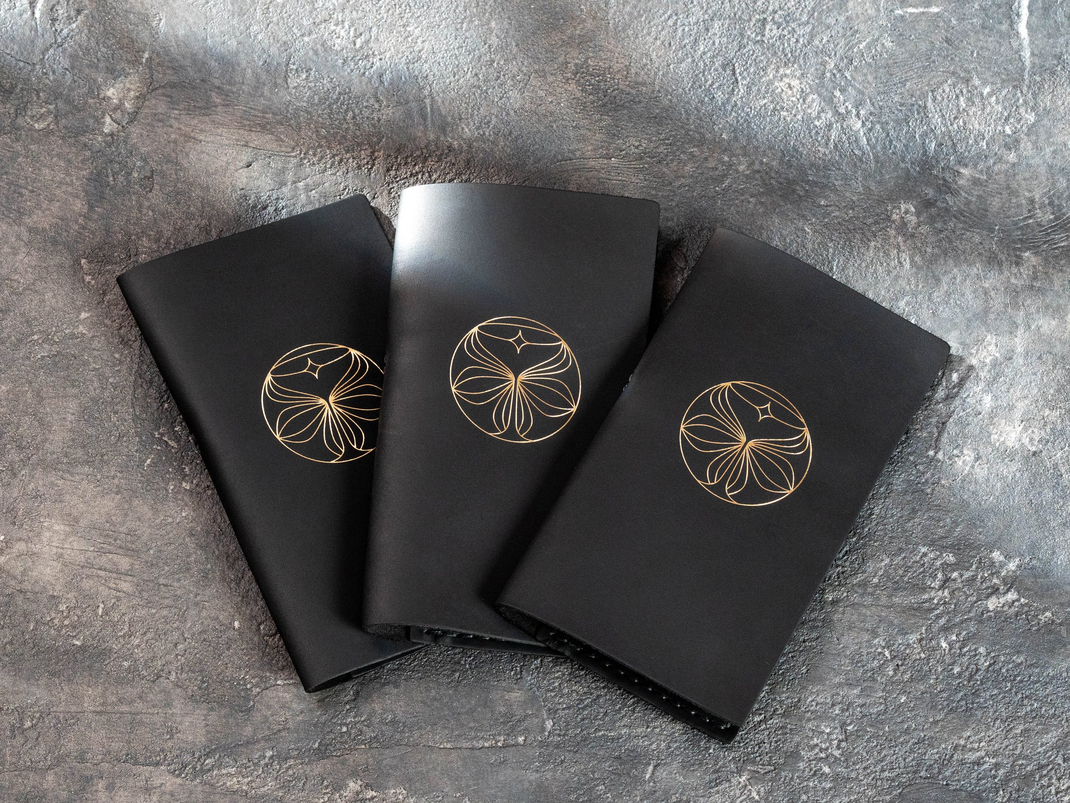 Three closed black leather restaurant check presenters personalized with matching gold foil logos