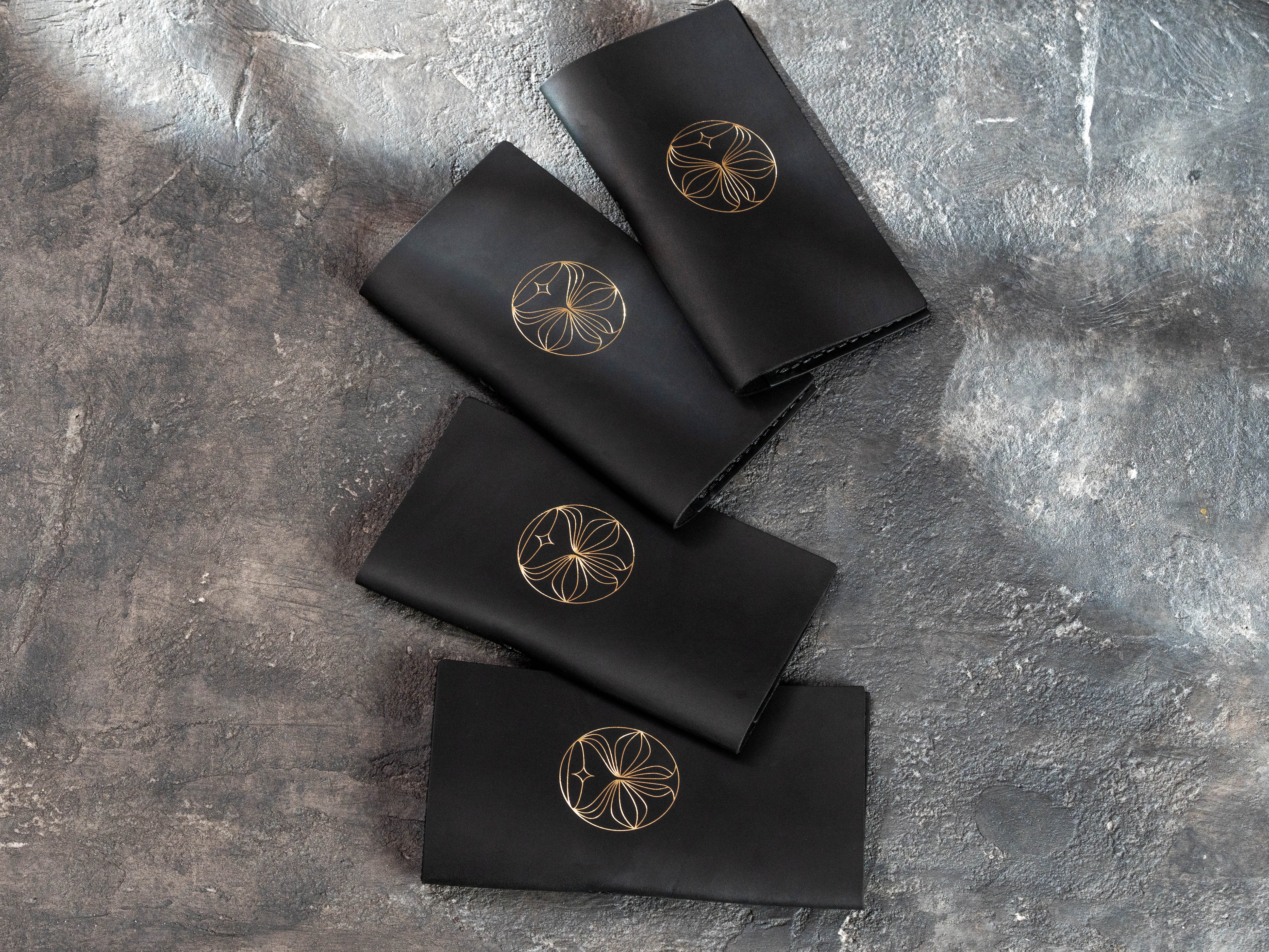 Four custom black leather bill holders with gold foil restaurant logos arranged on a textured background