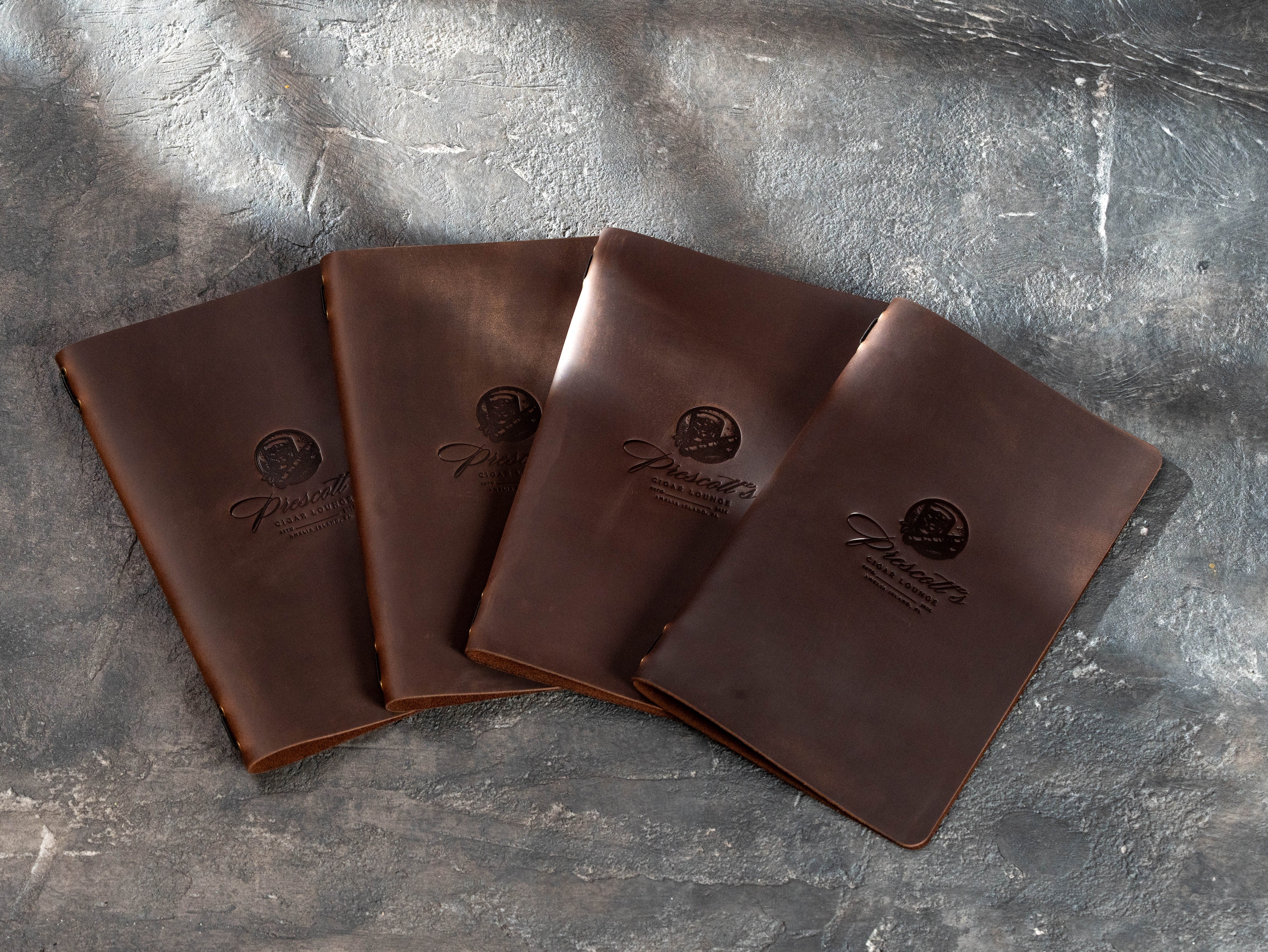 custom brown leather bar menu covers with embossed Prescott’s Cigar Lounge logos arranged on a textured background