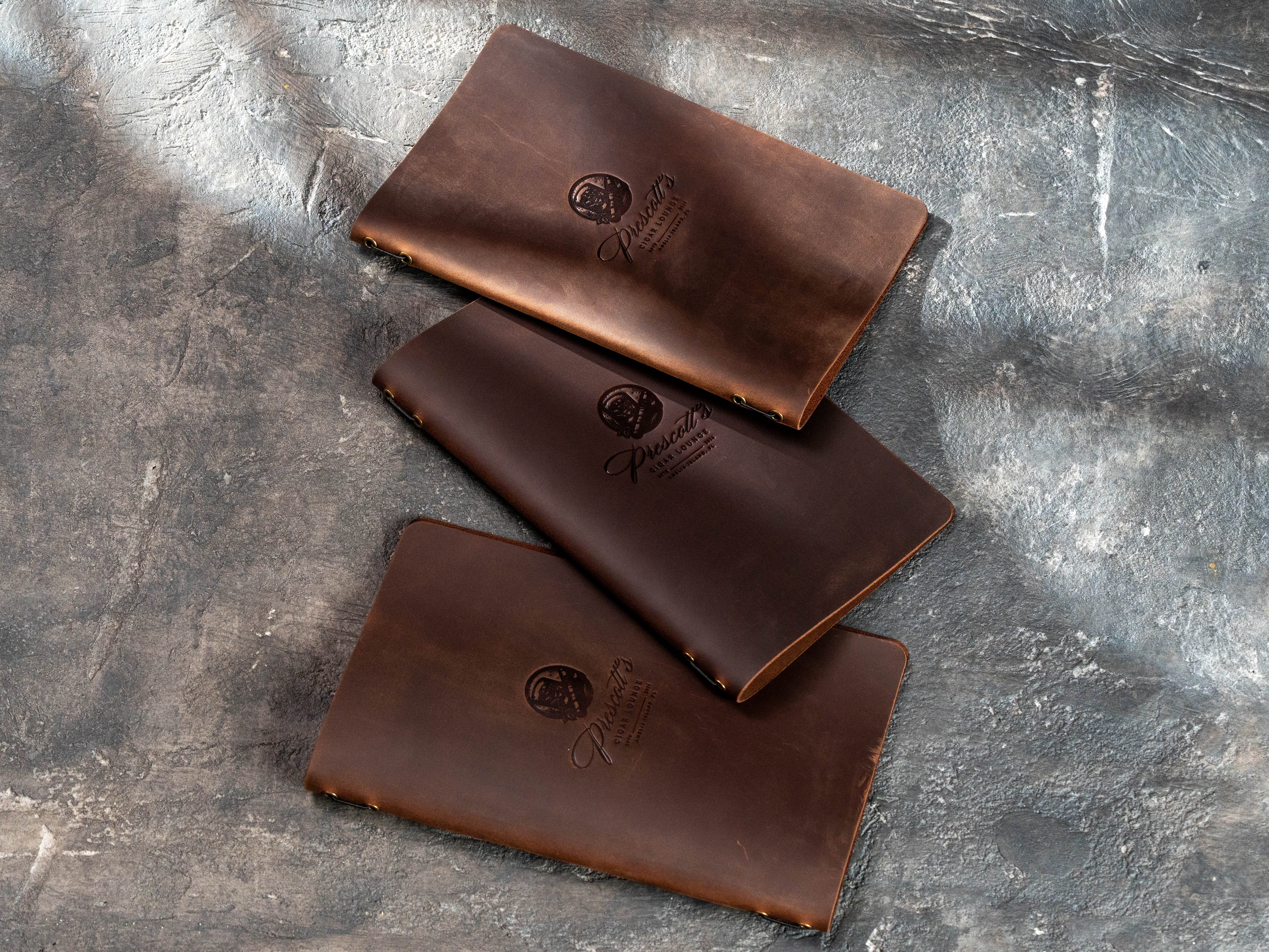 Three personalized brown leather menu covers with embossed cigar lounge logos and natural leather variations