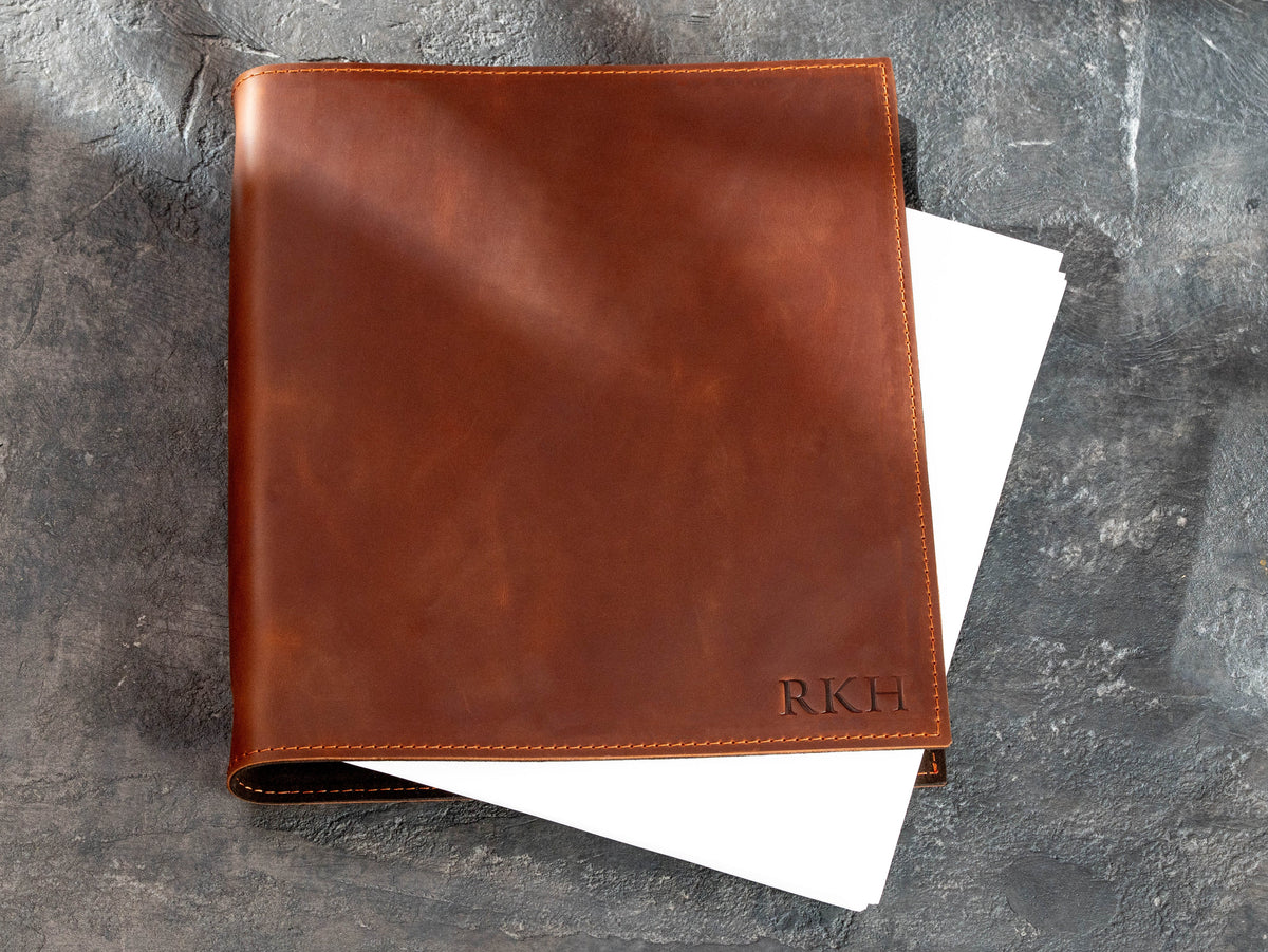 Copper leather 3-ring binder with custom initials and white document pages partially visible inside