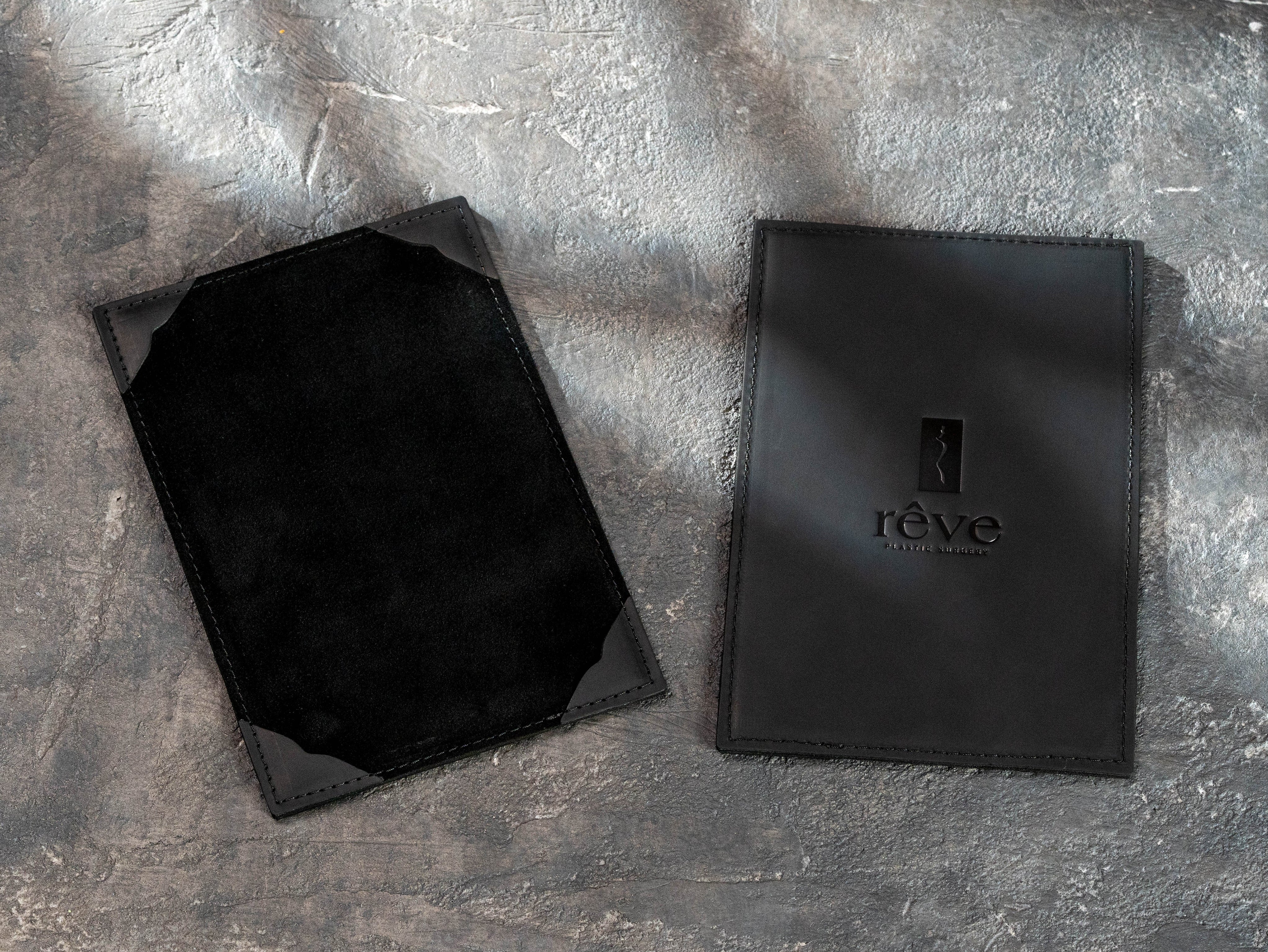 Black leather menu board with custom Rêve Bistro & Bar logo beside an open board with corner page holders