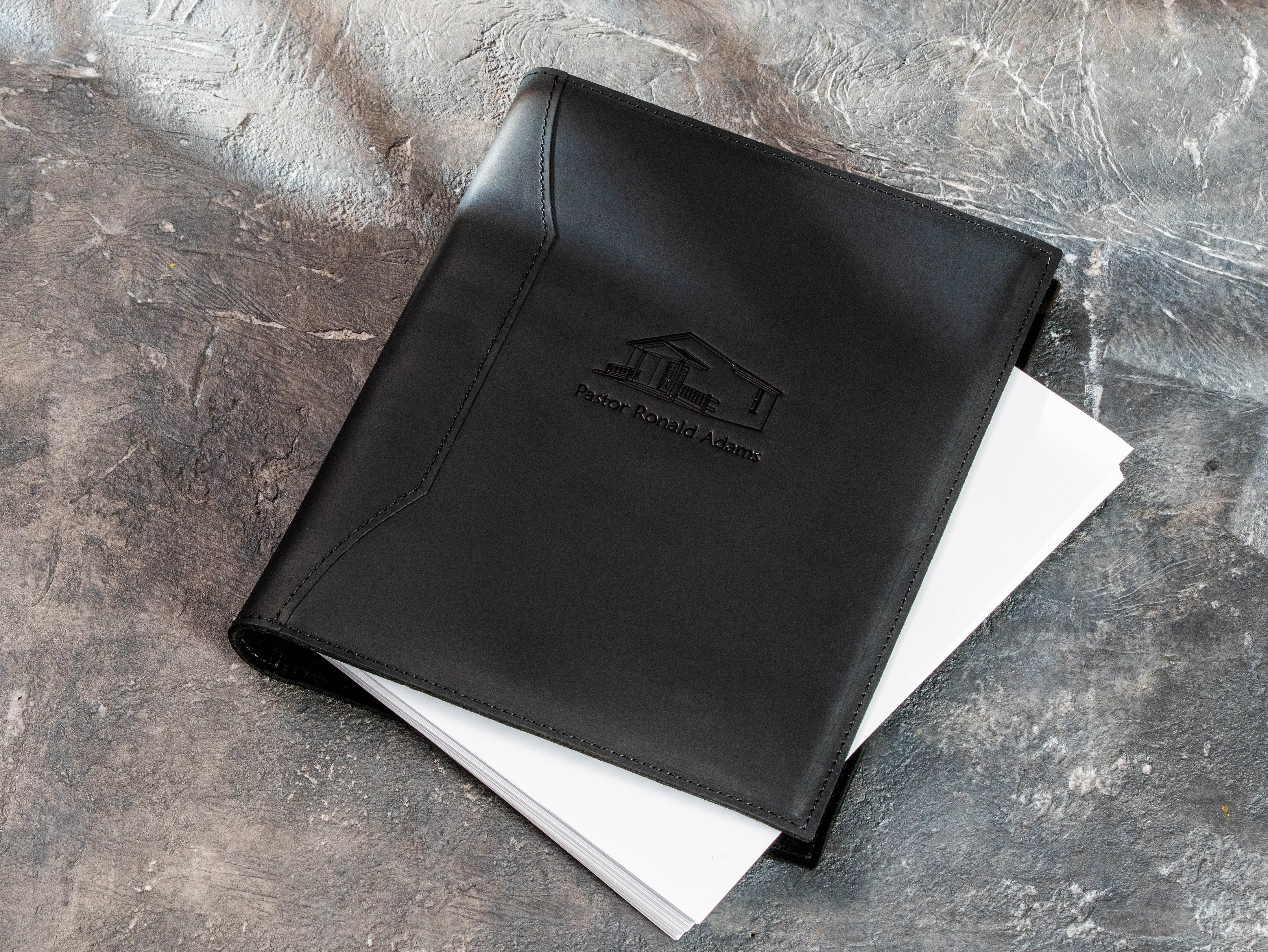 Black leather church document binder with open rings and a stack of Letter Size or A4 pages