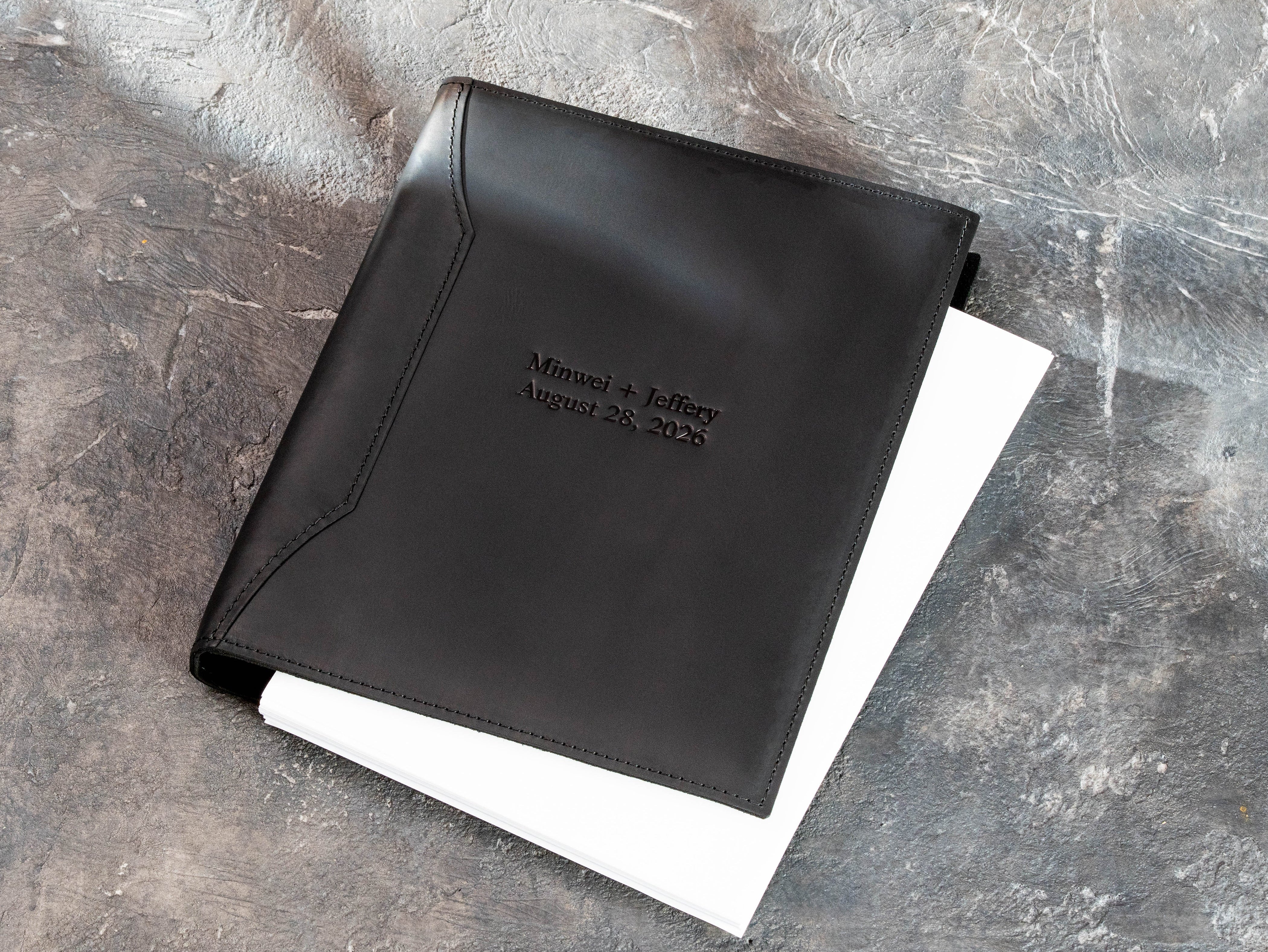 Open personalized black leather 3-ring wedding binder holding white paper pages