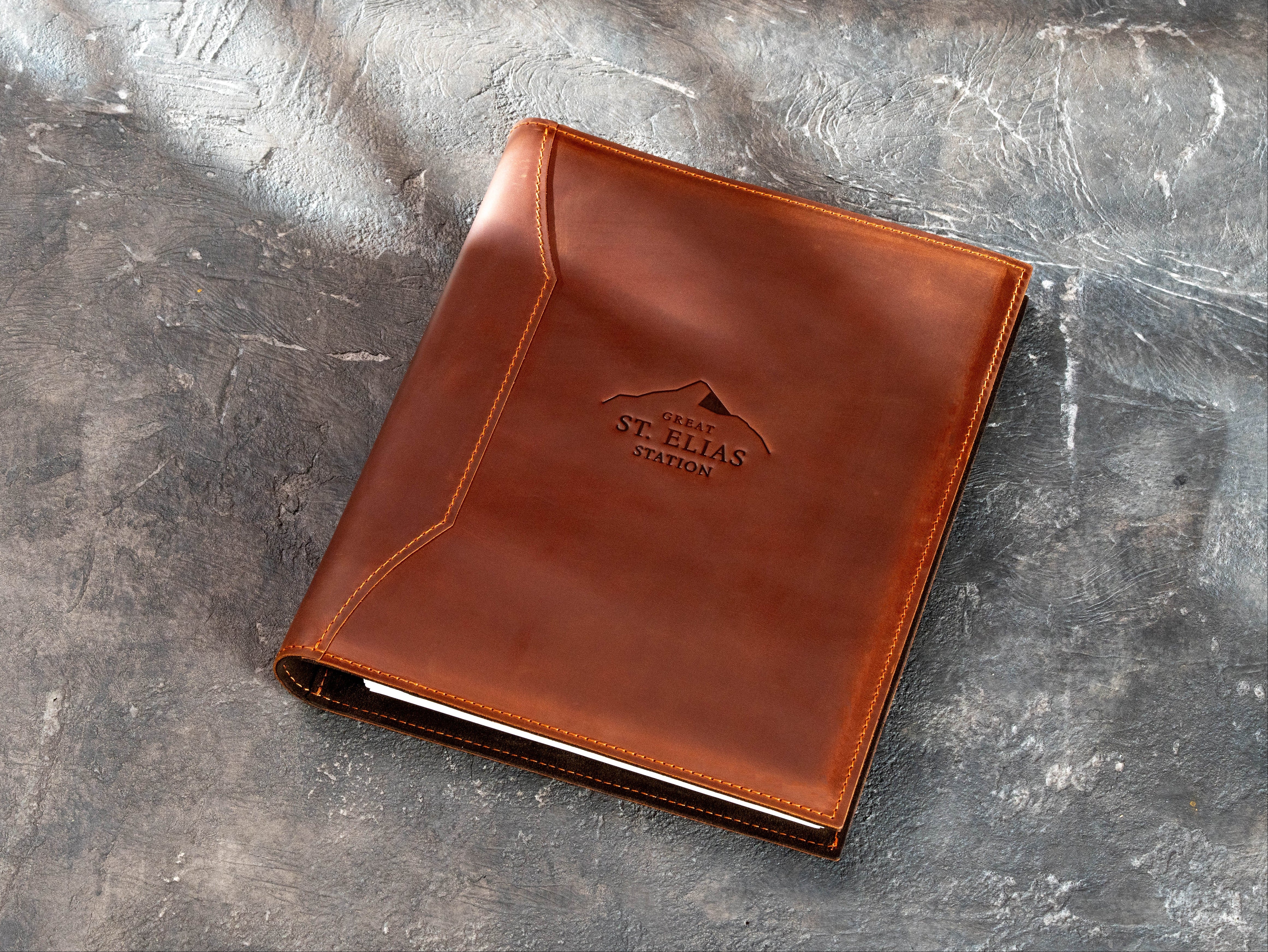 Closed Copper leather corporate binder with embossed Great St. Elias Station logo and decorative stitched cover