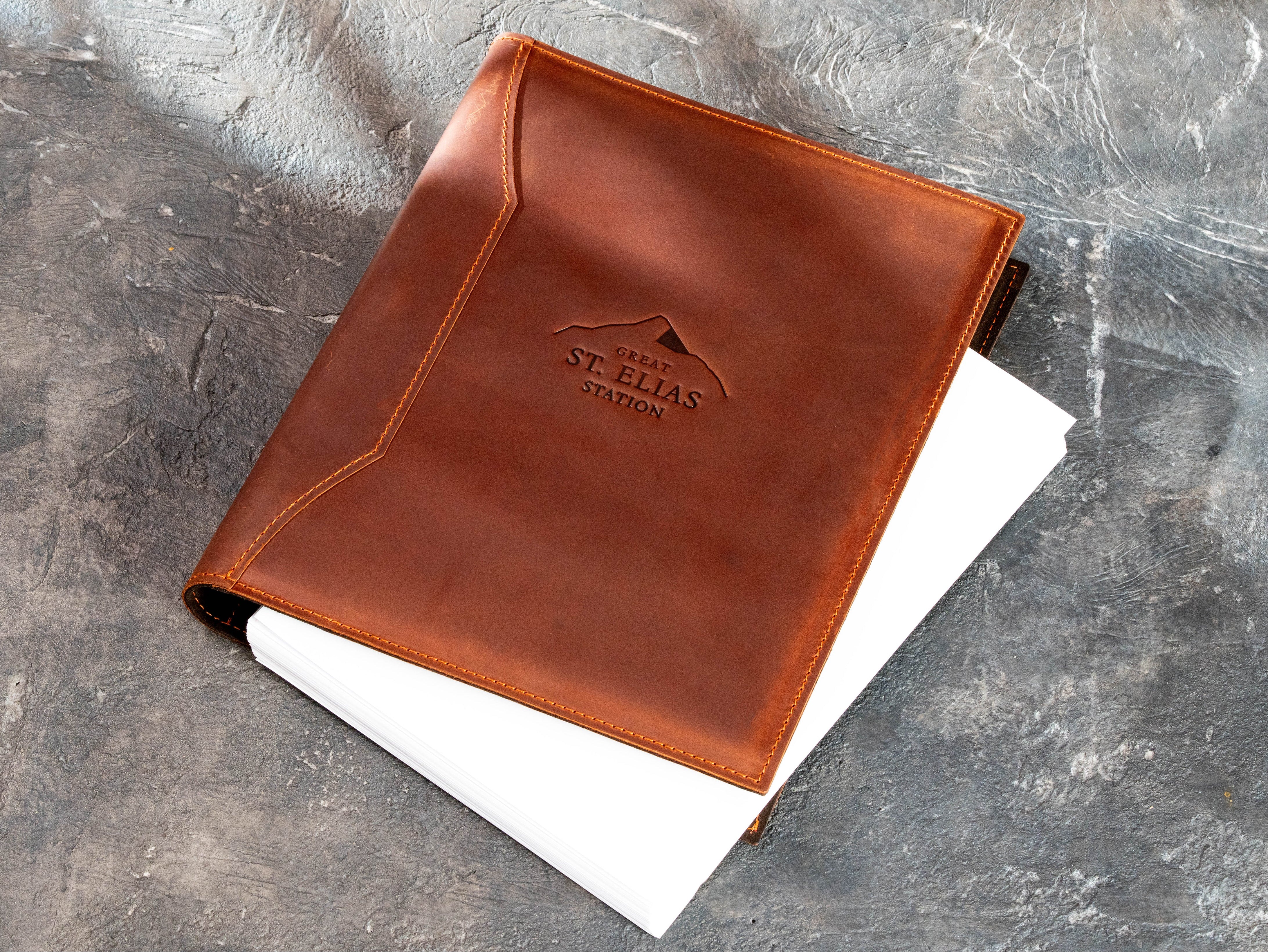 Copper leather corporate document binder with embossed company logo and white pages visible inside