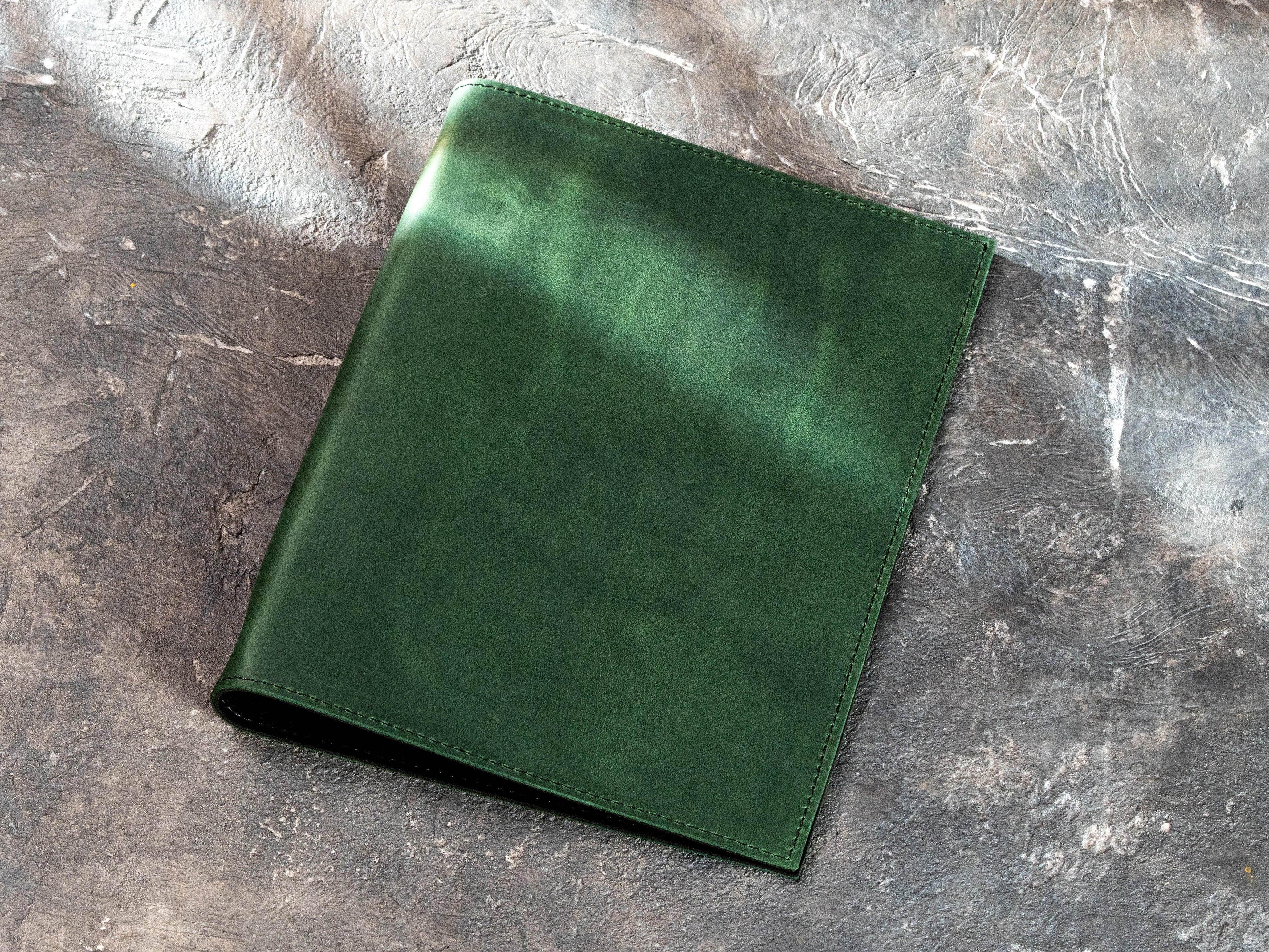 Green leather 3-ring binder without personalization showing natural tonal variations and stitched edges