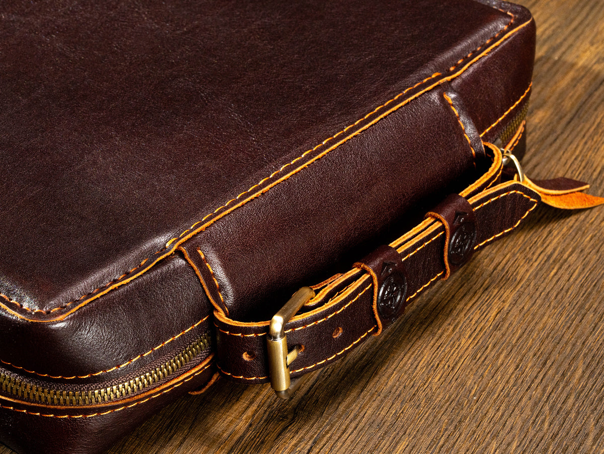 Dark Cognac leather travel organizer close-up with belt-style handle, compass details and hand saddle stitching