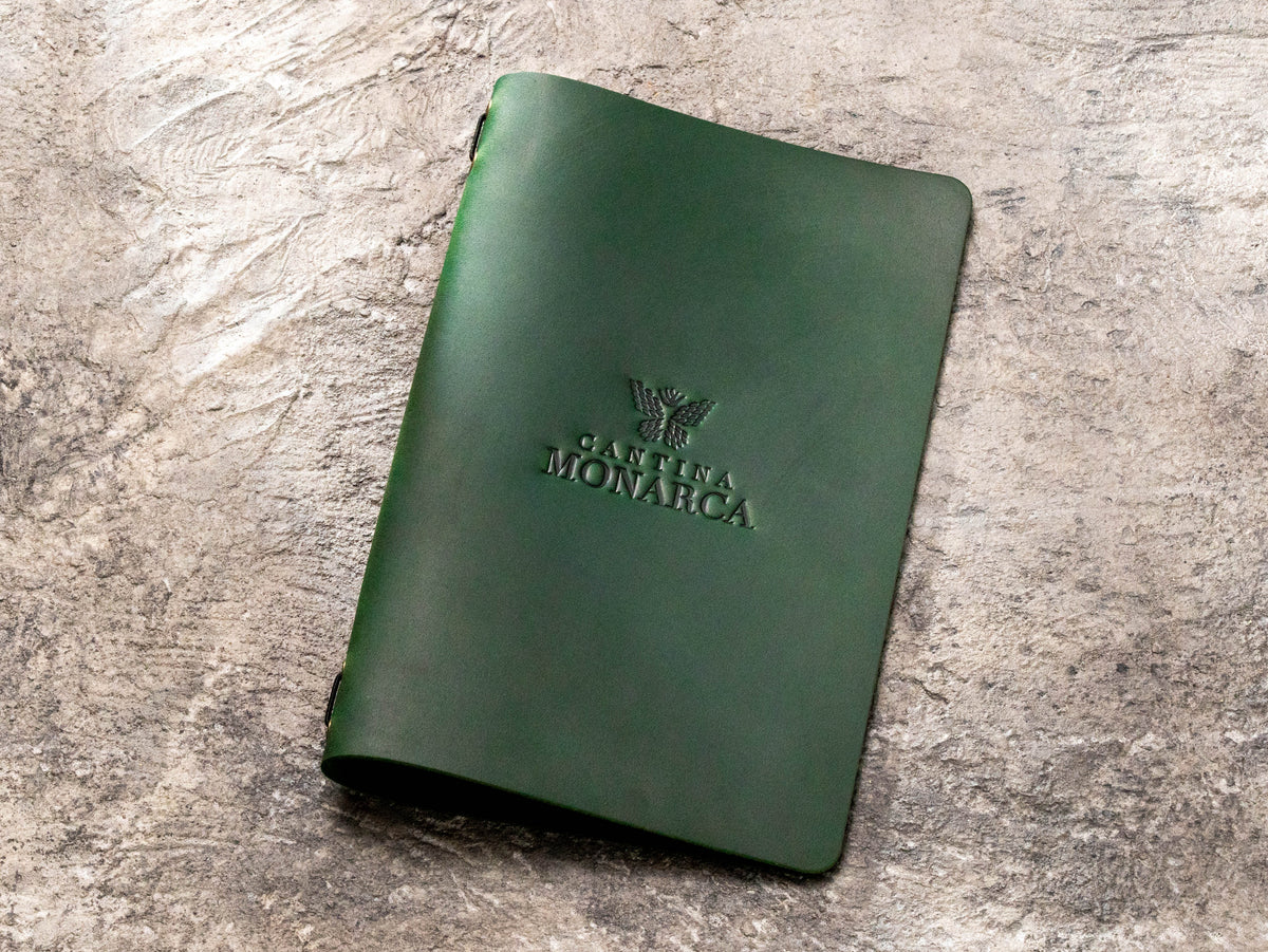 Dark green leather restaurant menu cover with blind embossed Cantina Monarca logo and elastic binding