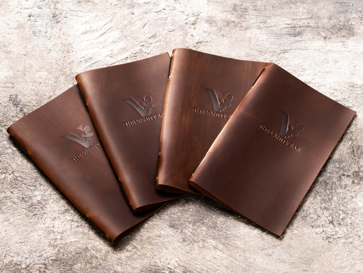 Custom brown leather service menu covers with The Vanity Bar logo for a med spa and beauty business