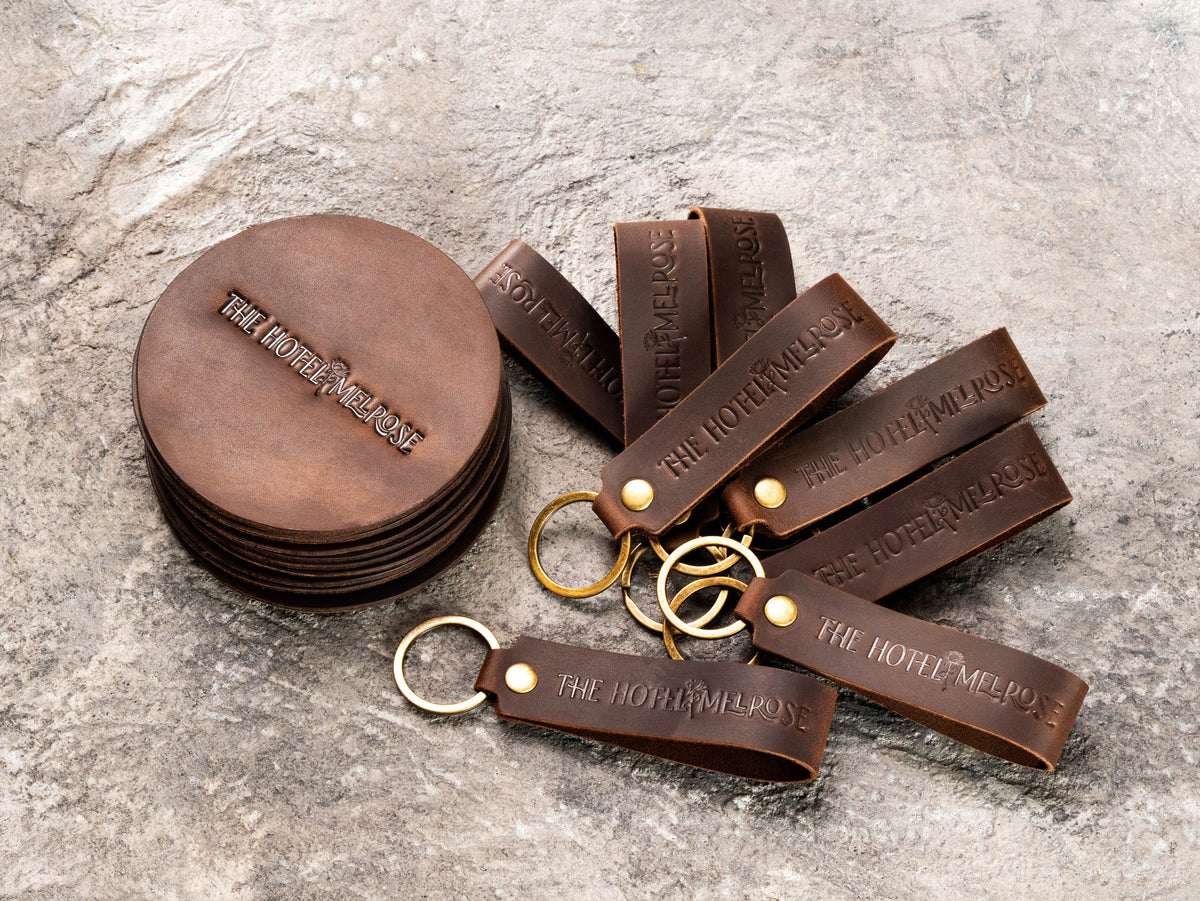 Bulk custom leather hotel keychains with embossed logo and antique brass-tone key rings for guest gifts