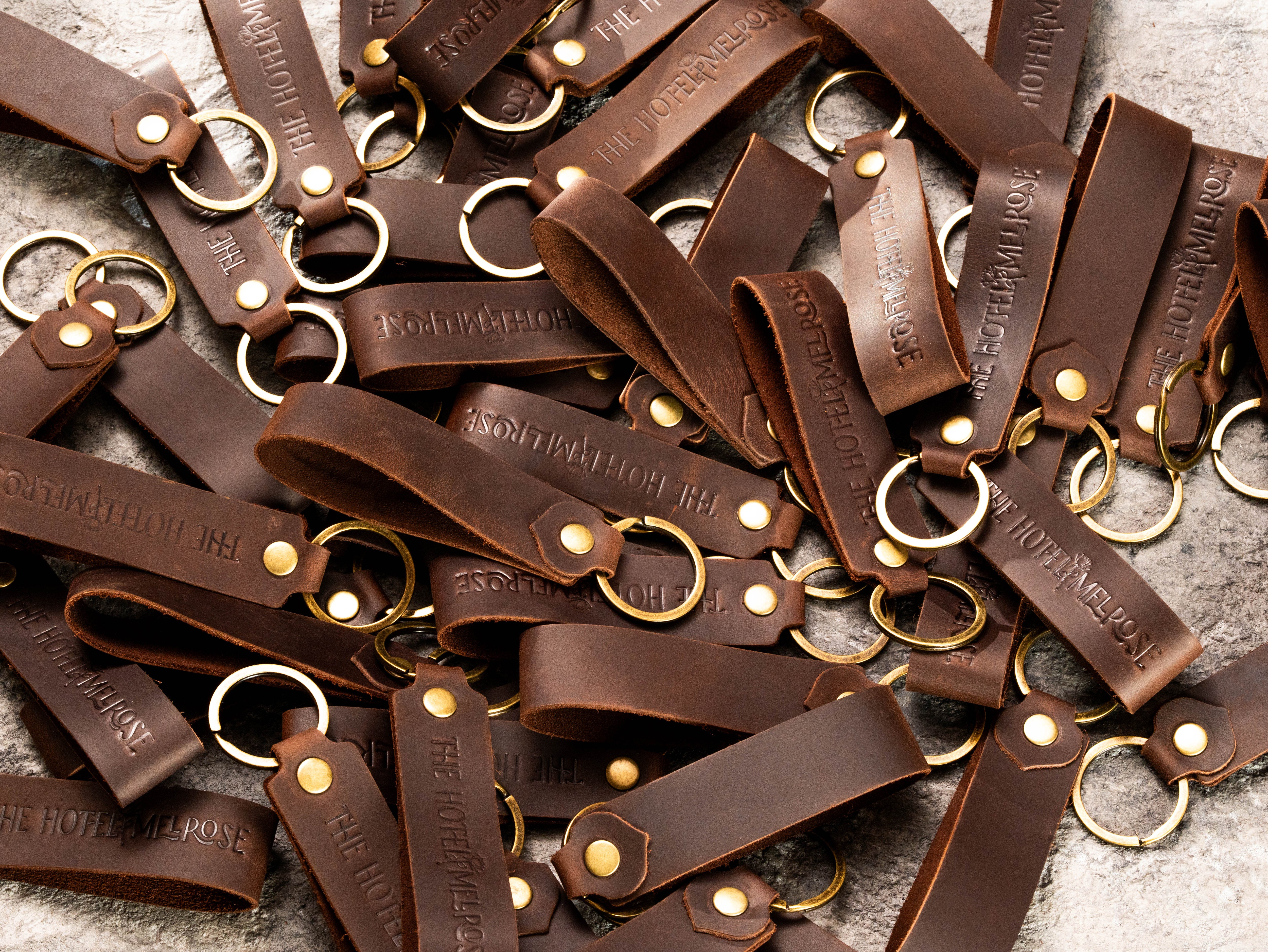 Custom brown leather hotel keychains with embossed The Hotel Melrose logo and matching leather coasters