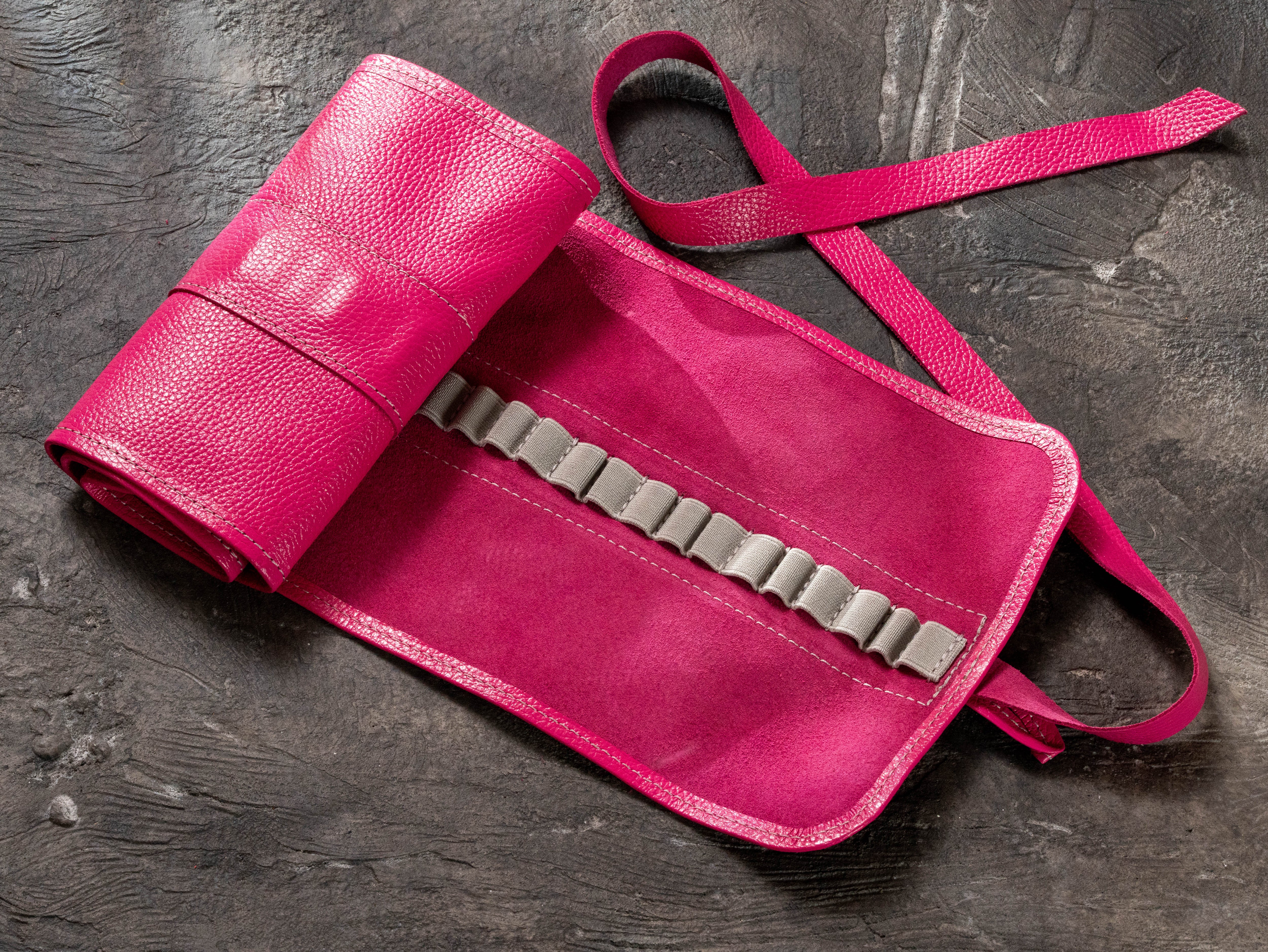 Bright pink leather pencil roll opened to show elastic holders and soft interior