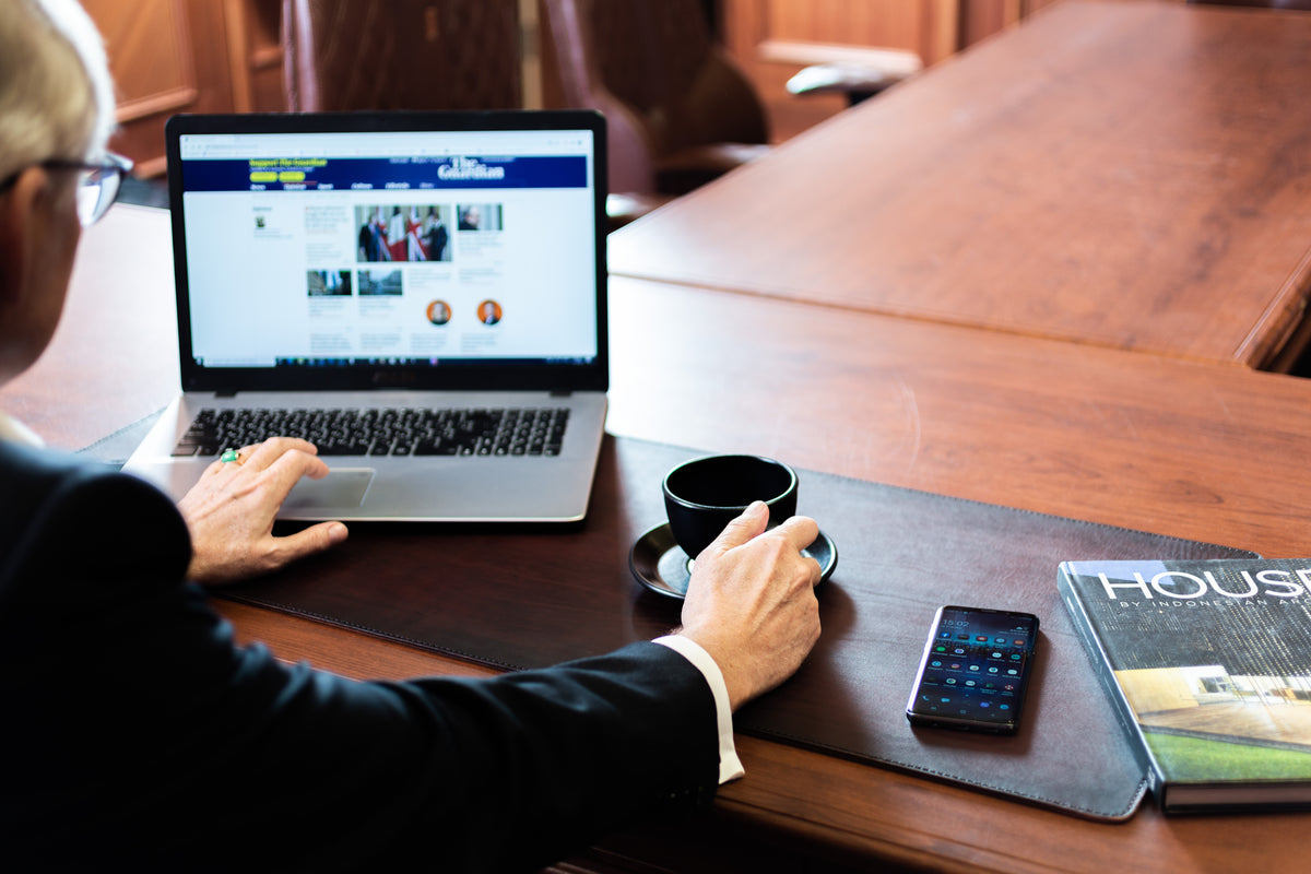 Copper leather desk mat with hand-aged dark perimeter used in executive office with laptop and smartphone
