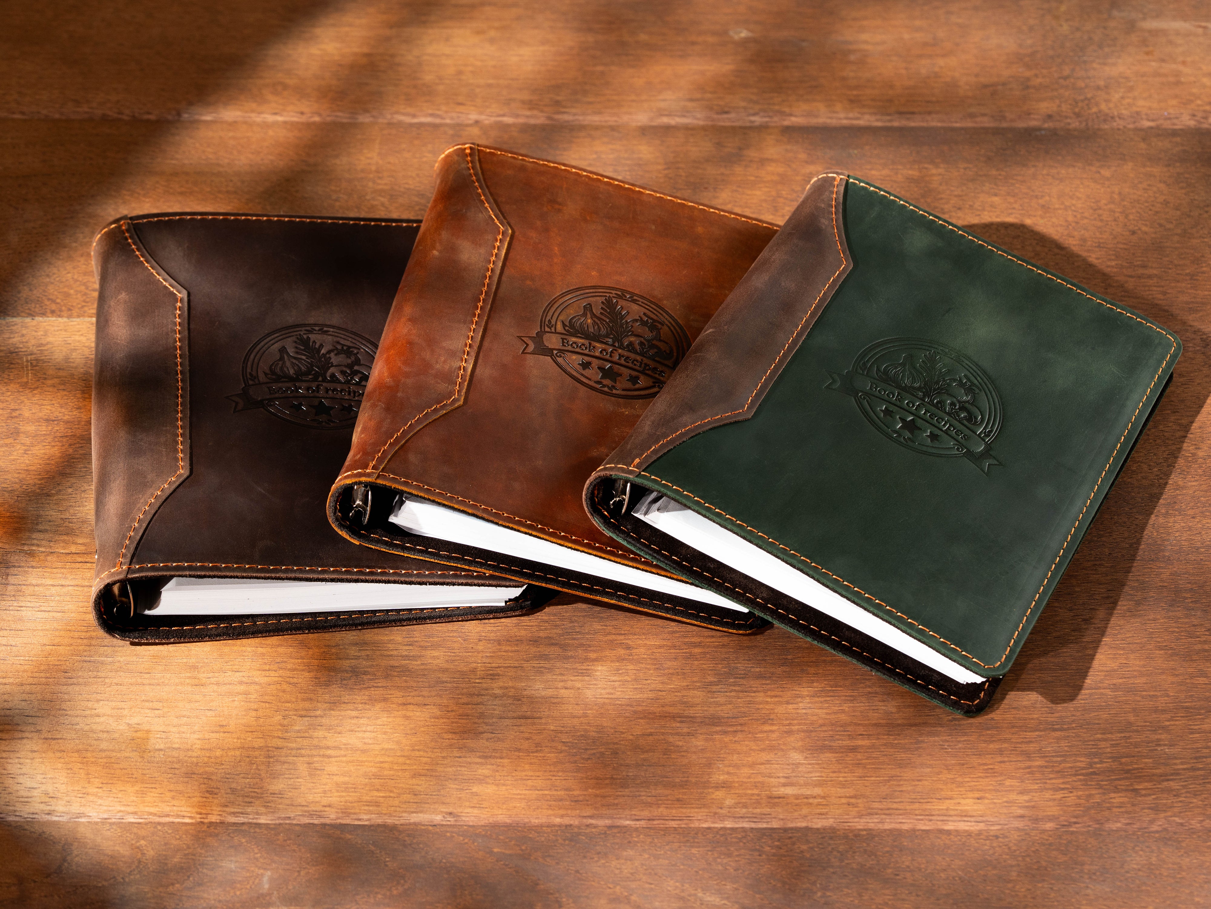 Three leather-bound notebooks in copper, brown, and green on a wooden surface.